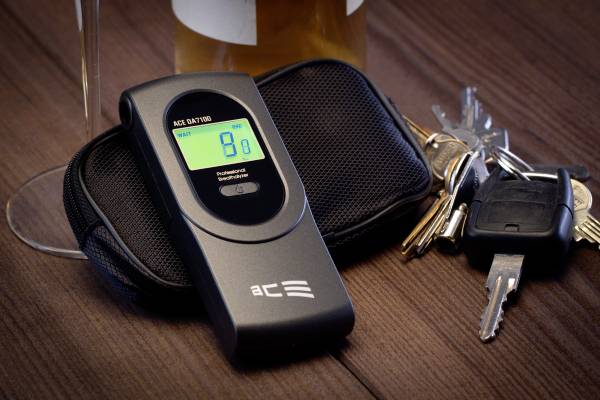 Alkoholtester mit digitalem Display zeigt '0.8' an, liegt neben einem Schlüsselbund, auf holzartiger Oberfläche.