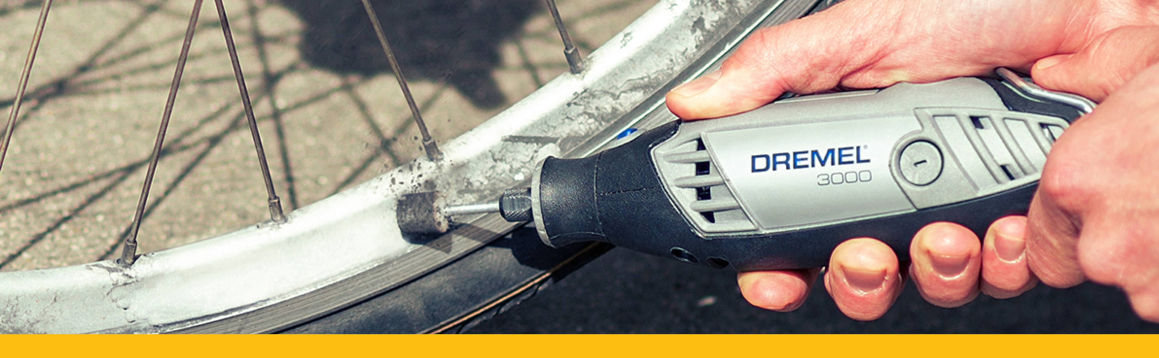Eine Hand hält ein Dremel-Werkzeug, das zum Schleifen des Fahrradfelgens verwendet wird. Der Fokus liegt auf dem präzisen Arbeitsvorgang.