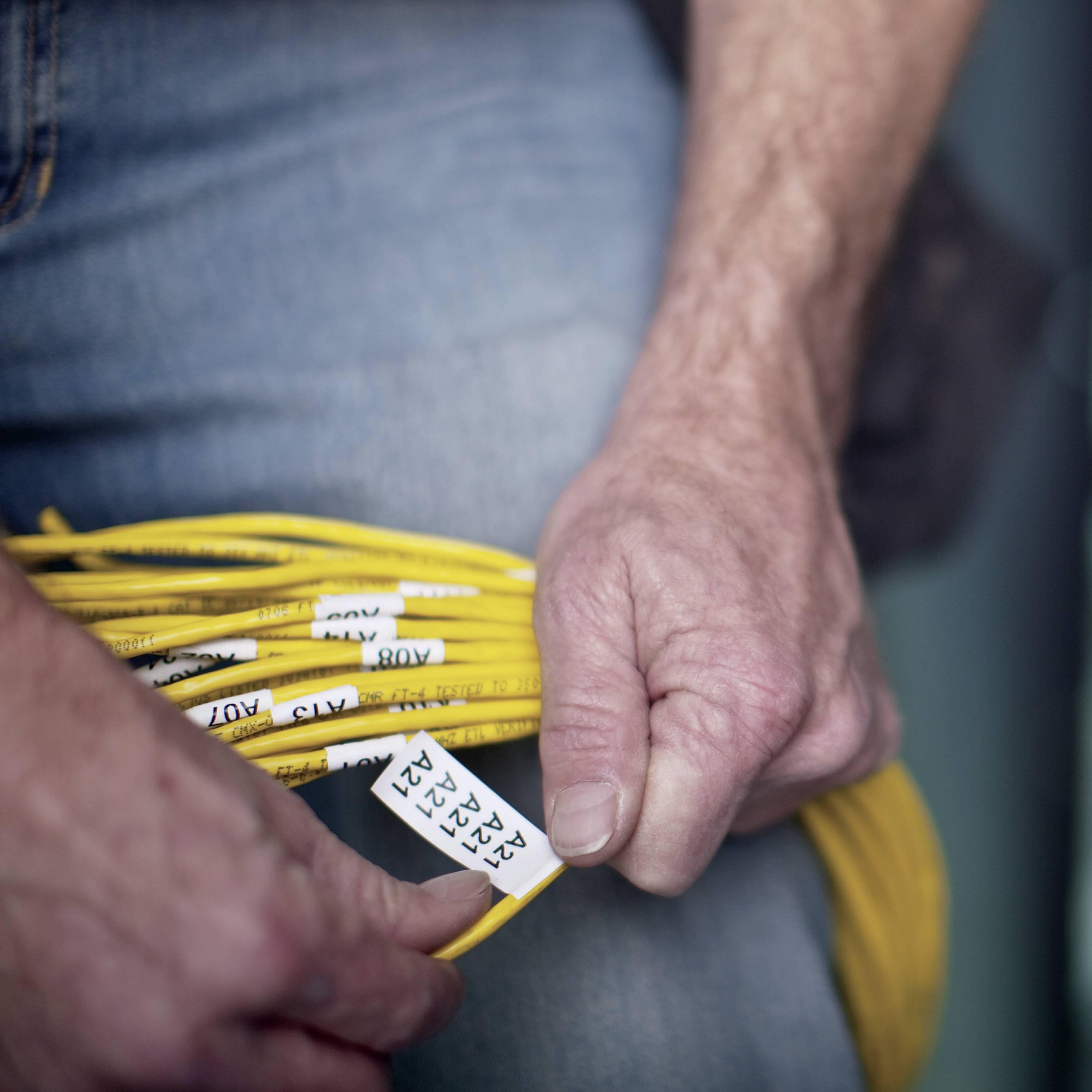 Eine Person hält ein gelbes Kabelbündel mit Etiketten in der Hand.