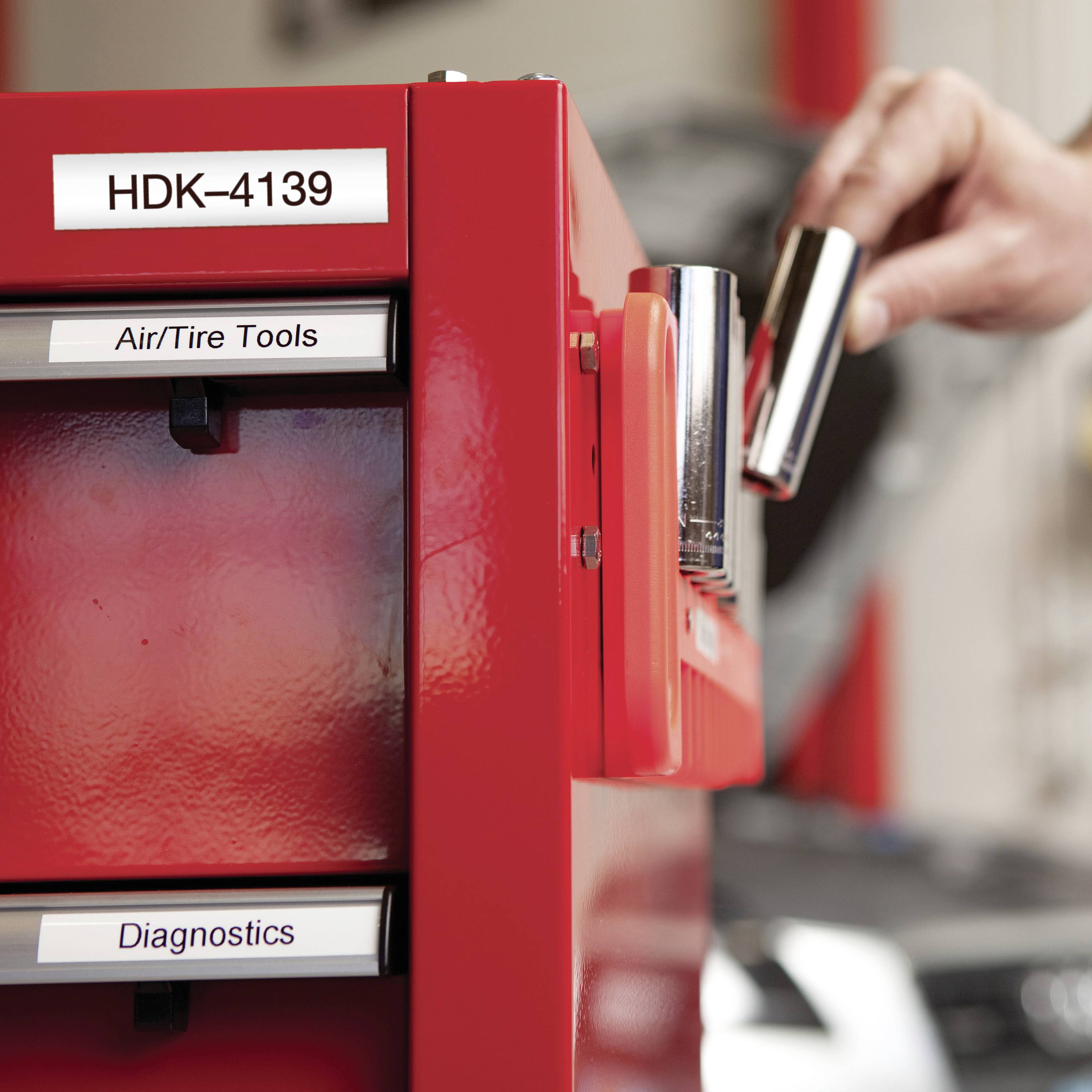 Eine Person greift nach einem Werkzeug aus einem roten Schrank mit den Etiketten 'Air/Tire Tools' und 'Diagnostics'.