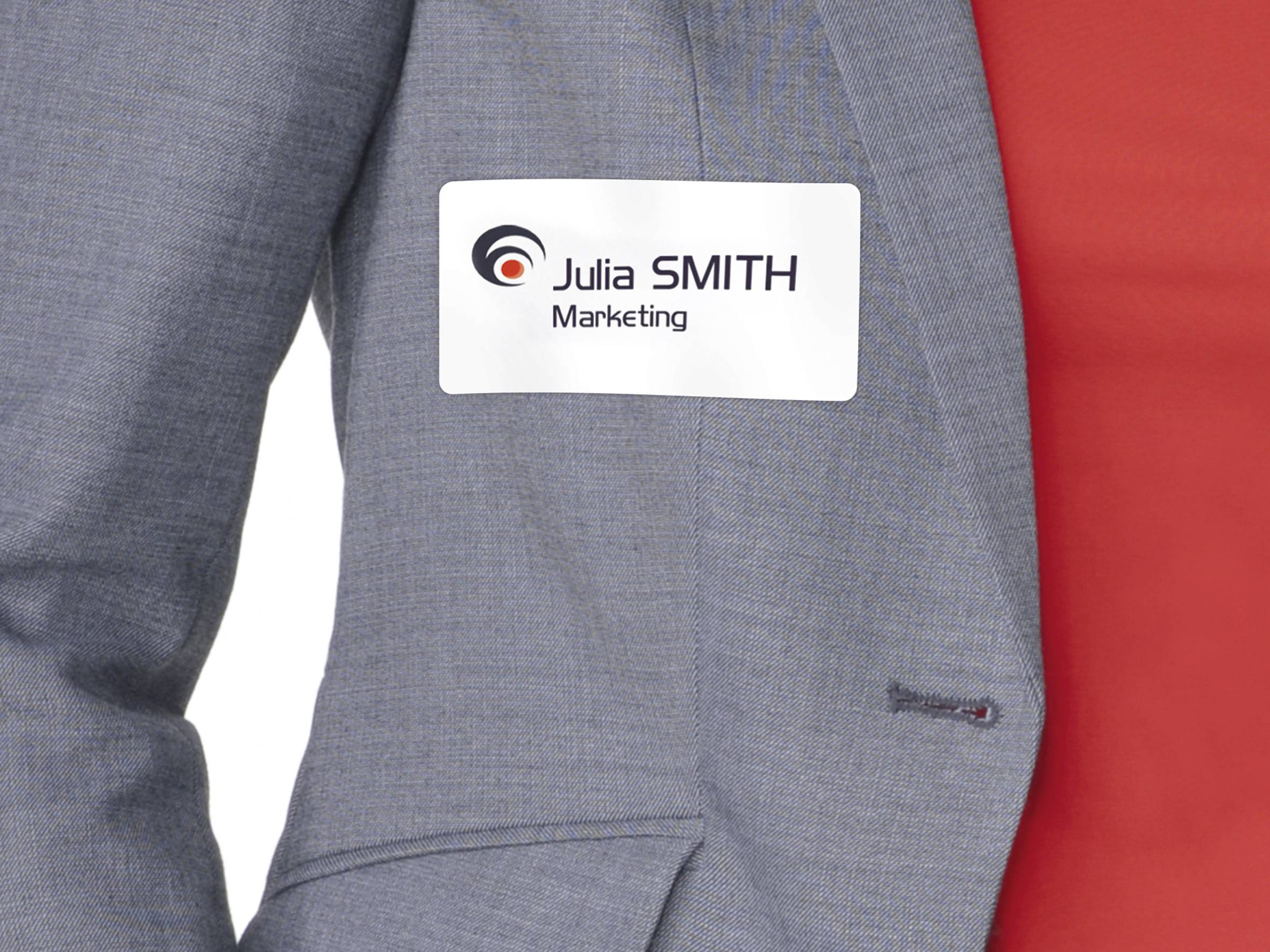 Person mit grauem Blazer trägt Namensschild mit Logo und der Aufschrift 'Julia SMITH Marketing'.