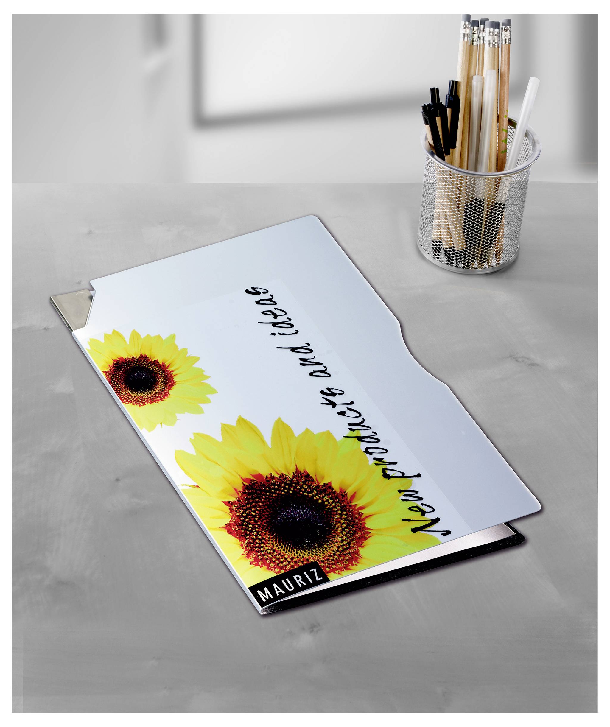 Personalisierte Schulmappe mit Sonnenblumenmotiv und Name 'Mauritz' auf grauem Tisch neben Stiftehalter.