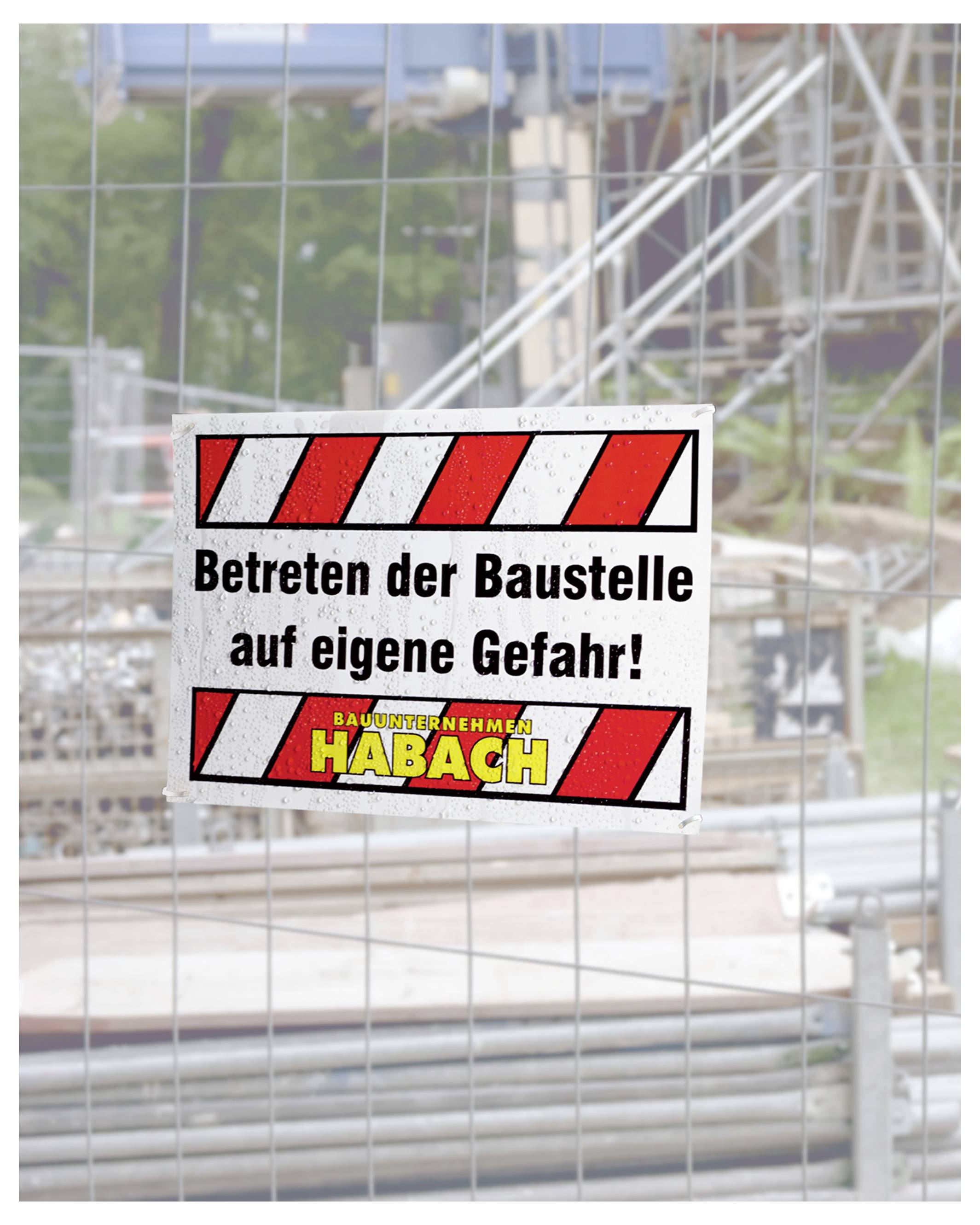 Warnschild an einem Bauzaun mit Text 'Betreten der Baustelle auf eigene Gefahr!'; im Hintergrund eine Baustelle mit Gerüst.
