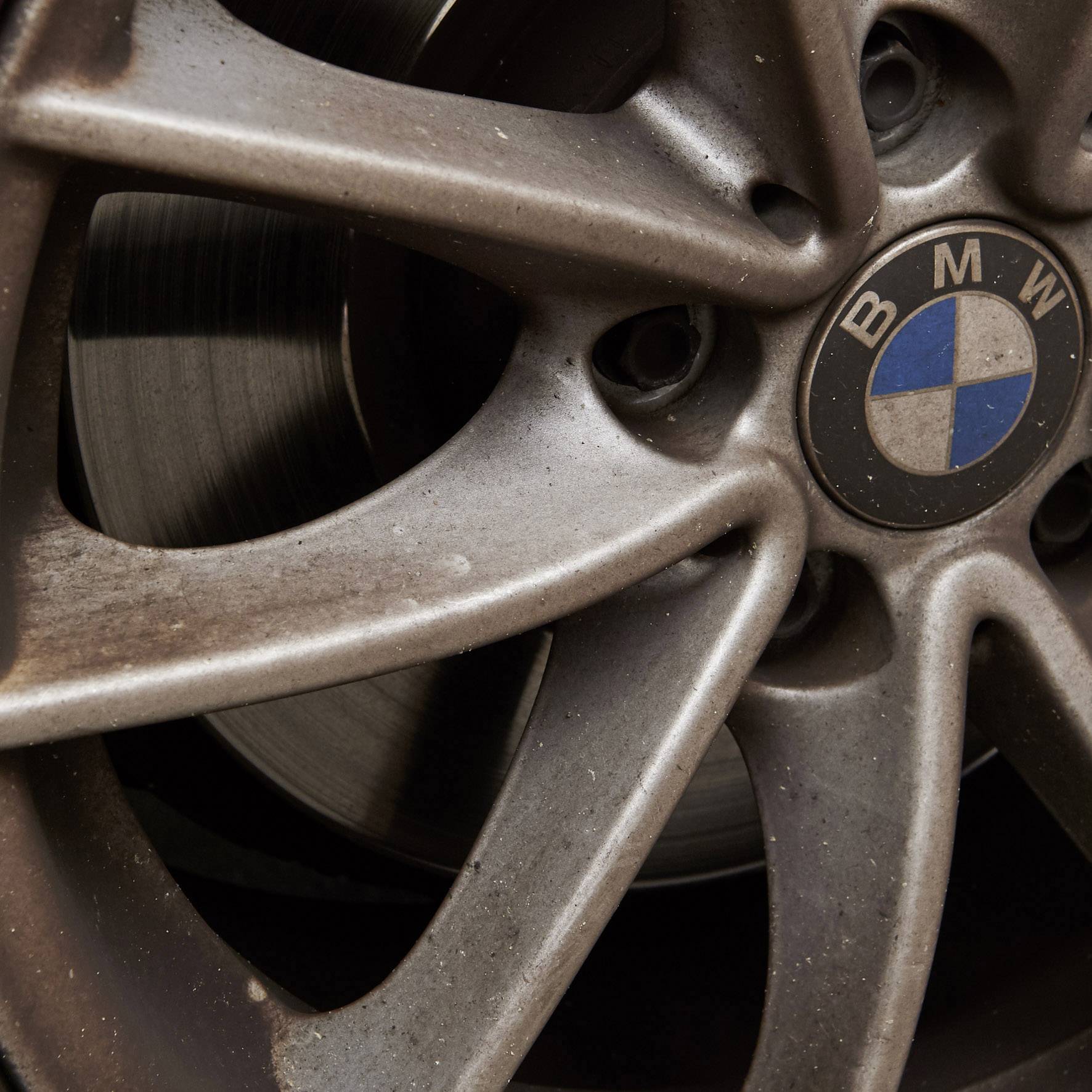Nahaufnahme einer schmutzigen BMW-Autofelge mit sichtbarem Logo in der Mitte.