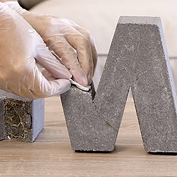 Eine behandschuhte Hand formt sorgfältig eine graue, betonähnliche Skulptur und glättet ihre Oberfläche mit einem Werkzeug, was einen Fokus auf Handwerkskunst andeutet.