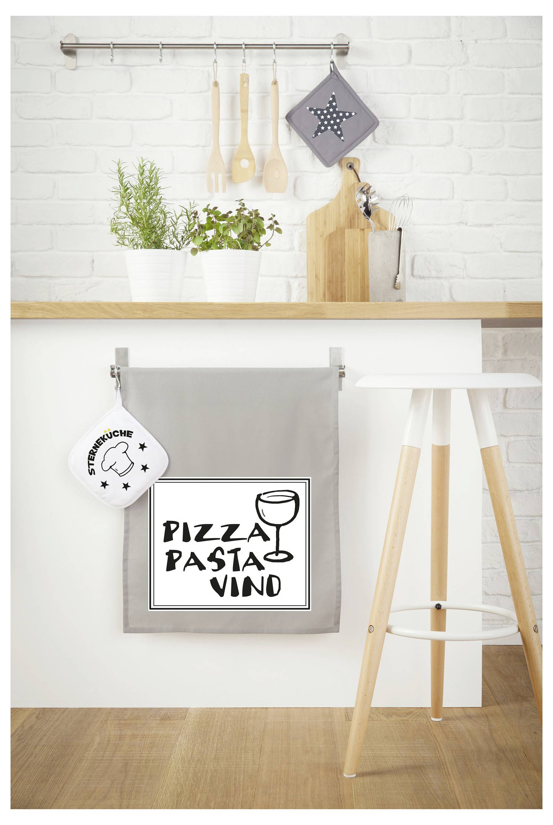 Küchendeko mit Hängeutensilien und Topfpflanzen; unten ein graues Tuch mit Schild 'PIZZA PASTA VINO' an einer Holzinsel.