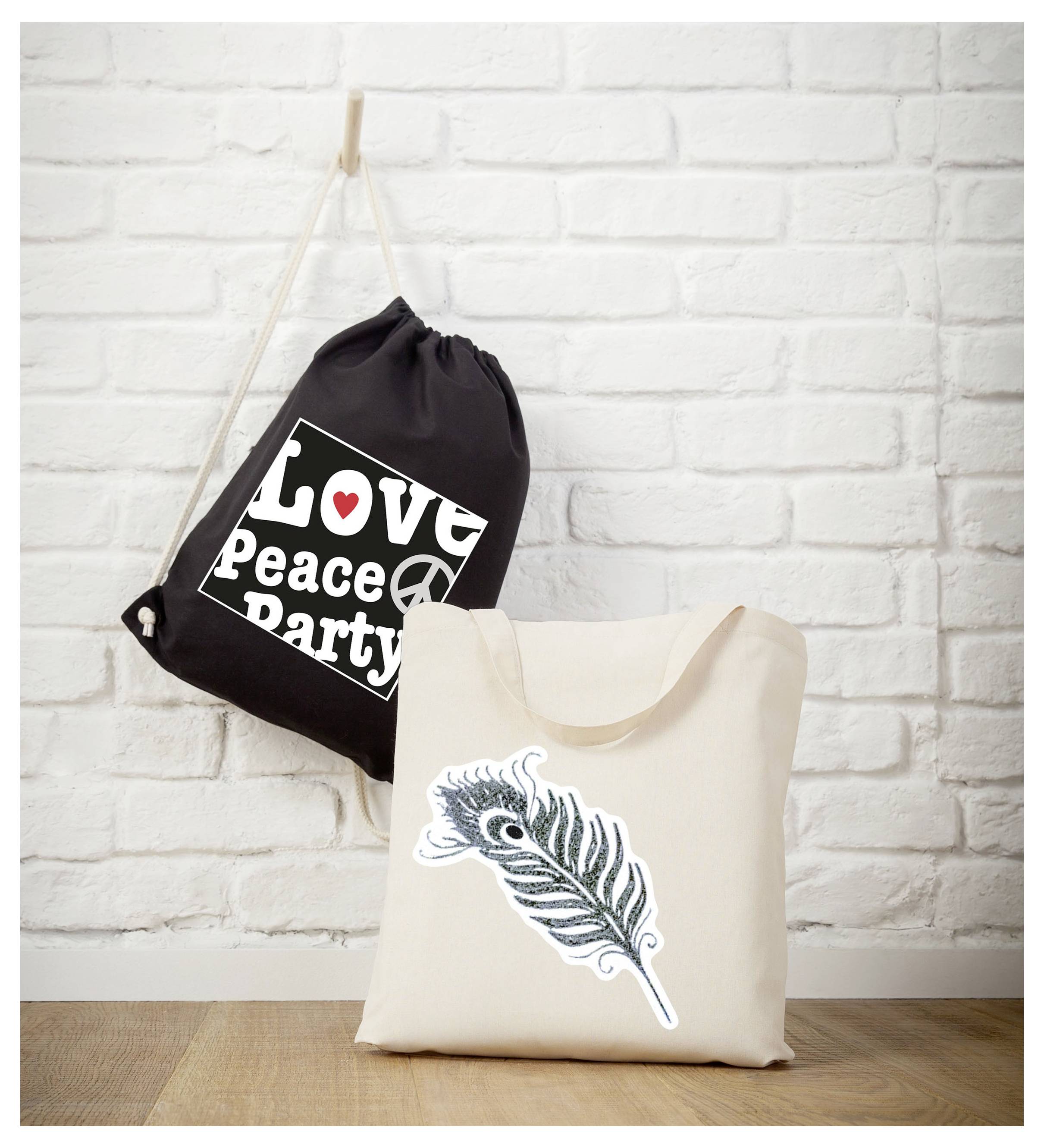 Zwei Stofftaschen vor weißer Ziegelwand: schwarze Beuteltasche mit Aufdruck 'Love Peace Party' und Creme-Tasche mit Feder-Motiv.