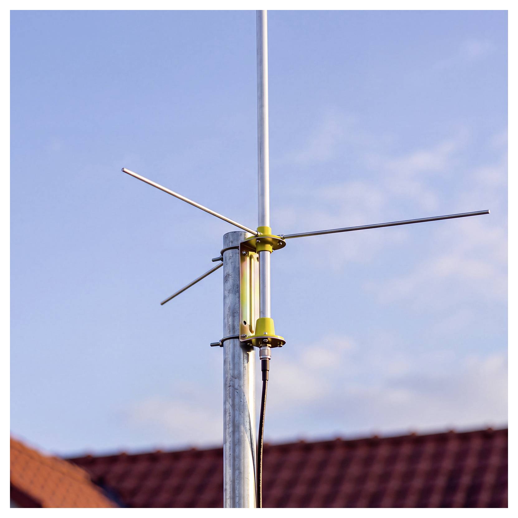 Eine auf einem Mast montierte Metallantenne vor blauem Himmel, mit darunter sichtbaren Dächern.