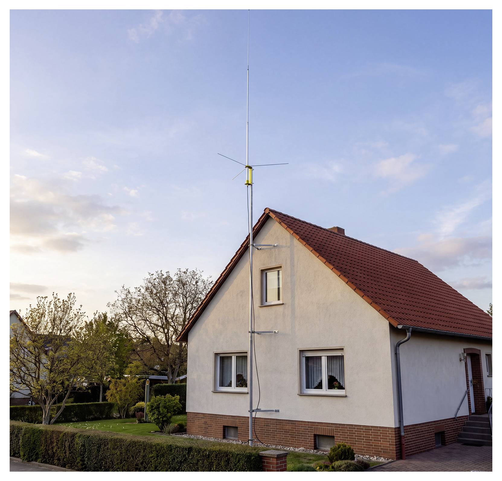 Ein Haus mit einer hohen Dachantenne oder einem Mast, der sich über das Dach gegen einen klaren Abendhimmel erhebt.