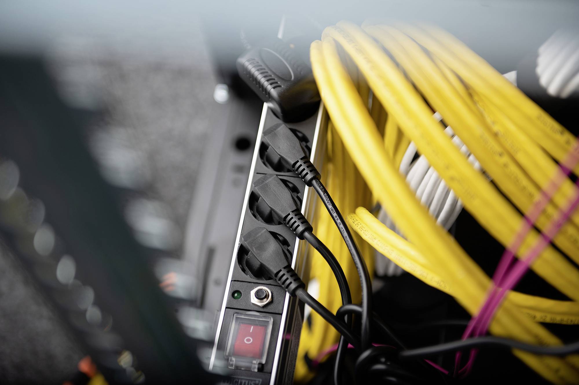 Ein schwarzer Mehrfachstecker mit vier angeschlossenen Kabeln neben gelben Kabeln, wahrscheinlich in einem Technik- oder Serverraum.