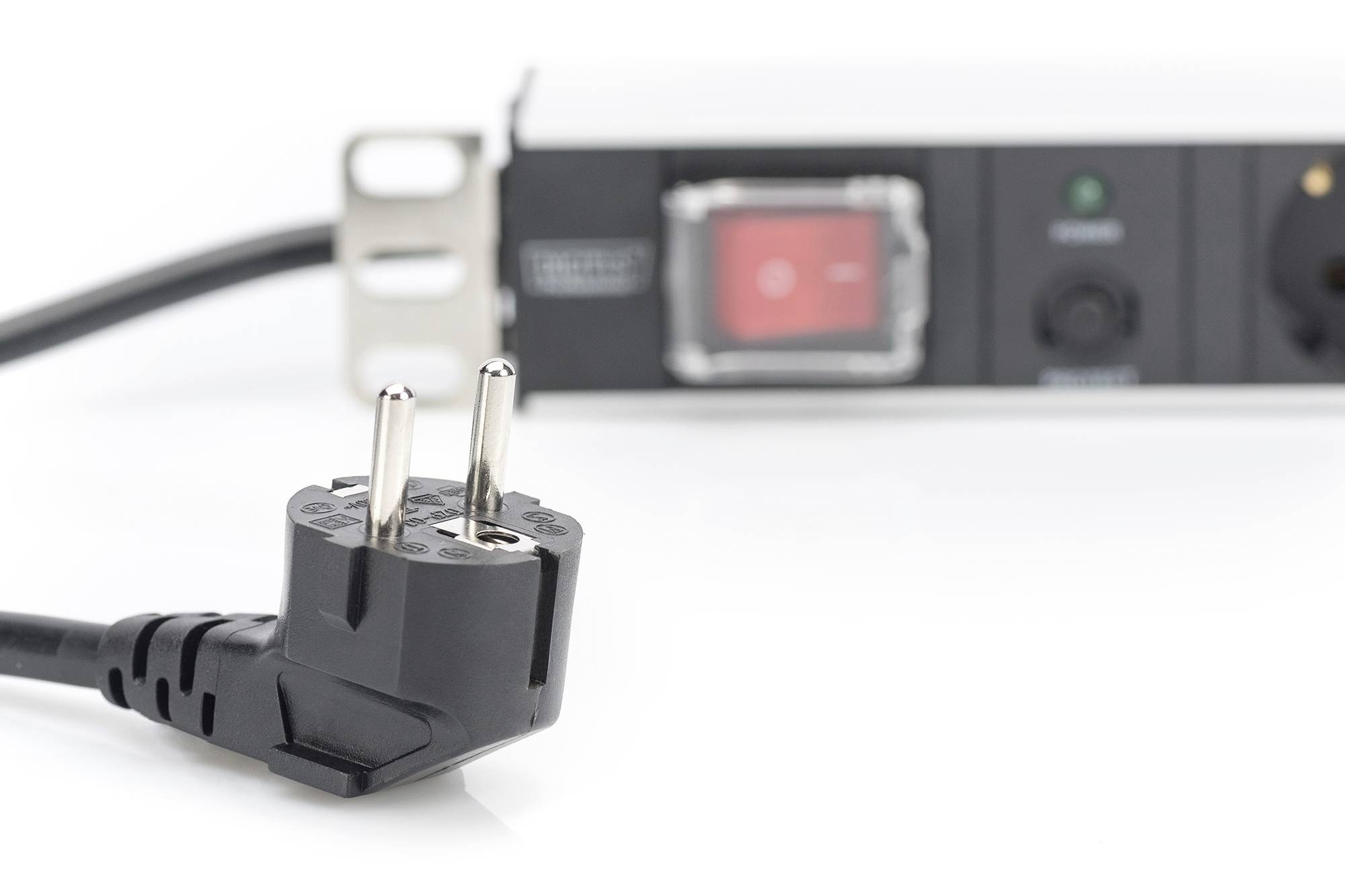 Schwarzer Schukostecker im Vordergrund, unscharfe Steckdosenleiste mit Kippschalter im Hintergrund. Symbolisiert Elektrizität und Anschlussmöglichkeiten.