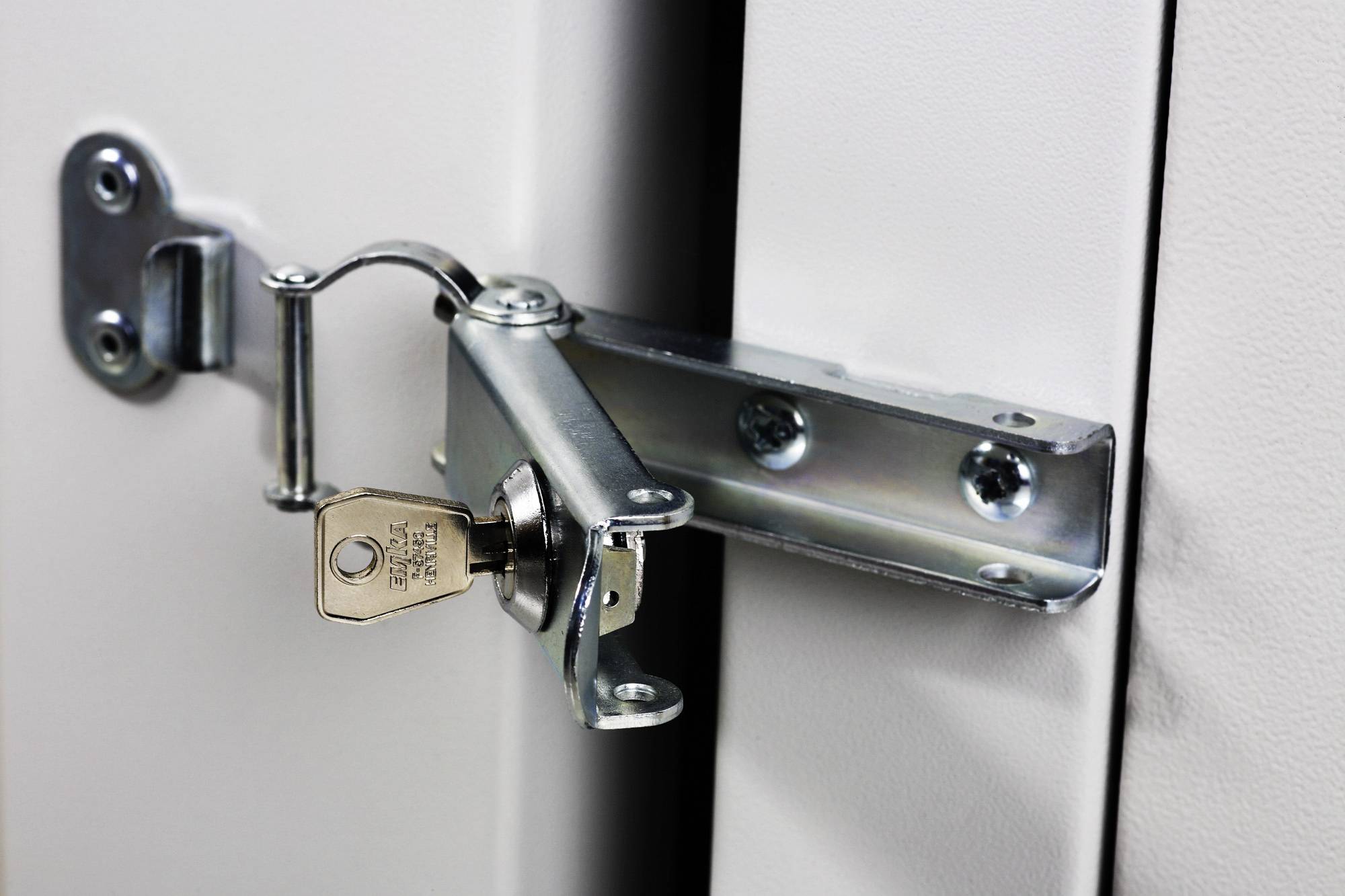 Ein Metallschrank mit einem Riegelschloss, der mit einem Schlüssel verschlossen ist. Der Schrank ist weiß und aus Metall gefertigt.