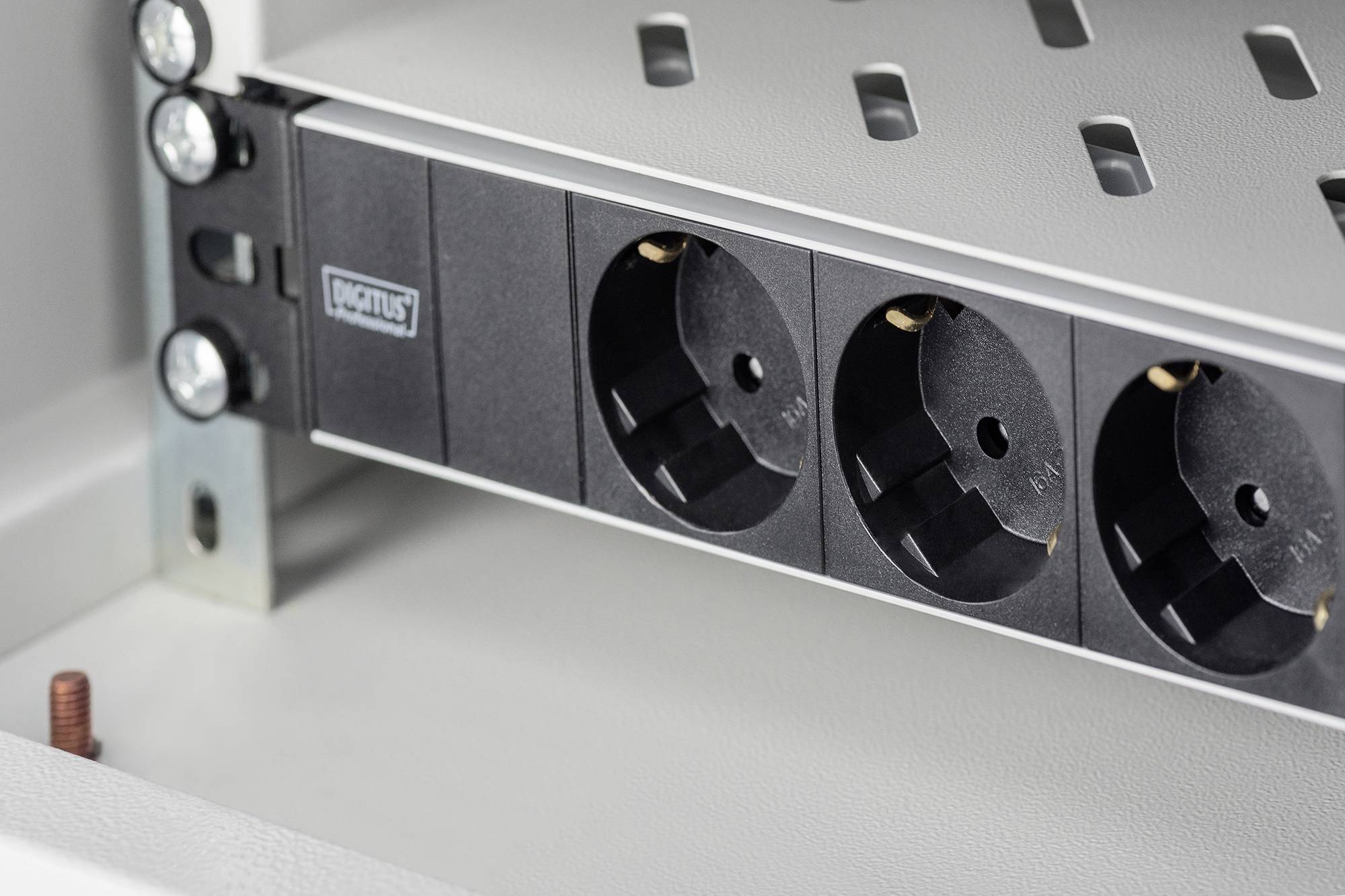 Ein schwarzes Steckdosenmodul mit drei Schutzkontakt-Steckdosen ist in ein graues Metallregal eingebaut.