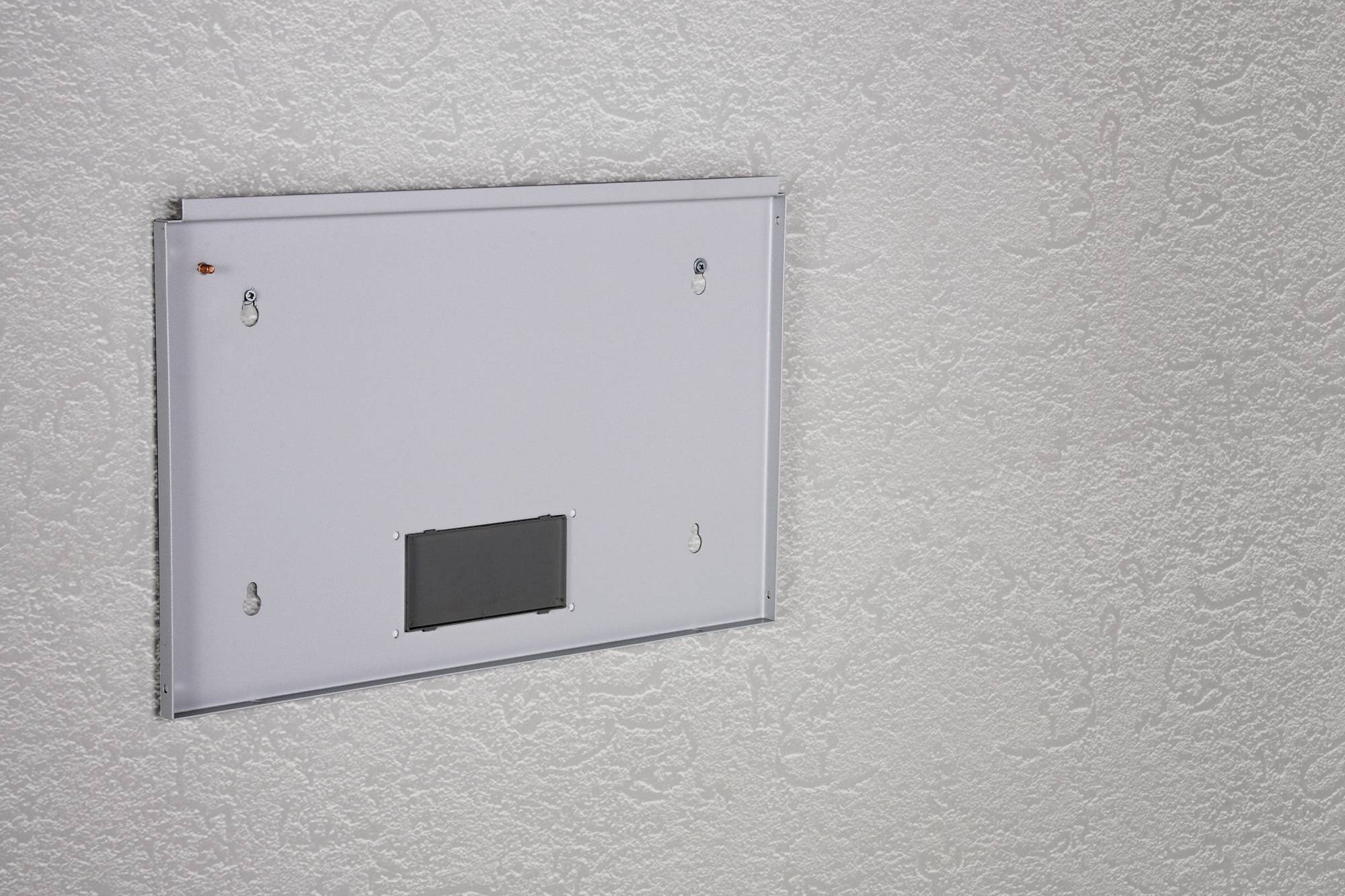 Eine weiße Heizplatte ist an einer strukturierten grauen Wand montiert. Sie ist minimalistisch gestaltet ohne sichtbare Steuerungselemente.