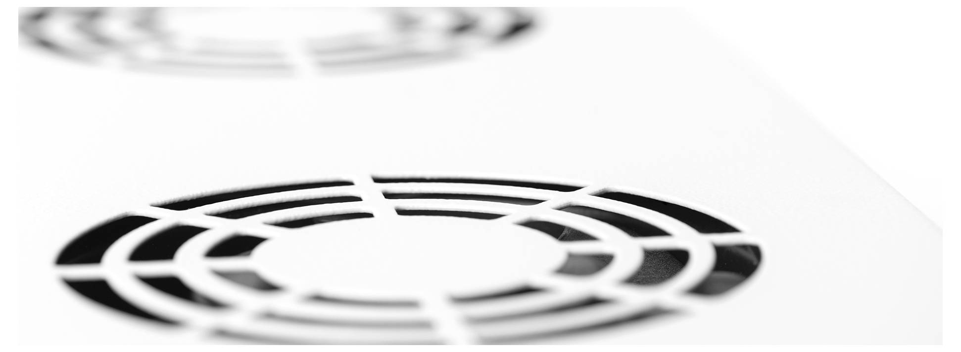 Nahaufnahme von zwei kreisförmigen Lüftungsgittern auf einer flachen weißen Oberfläche, teilweise unscharf, mit Fokus auf das Lüftungsgitter im Vordergrund.