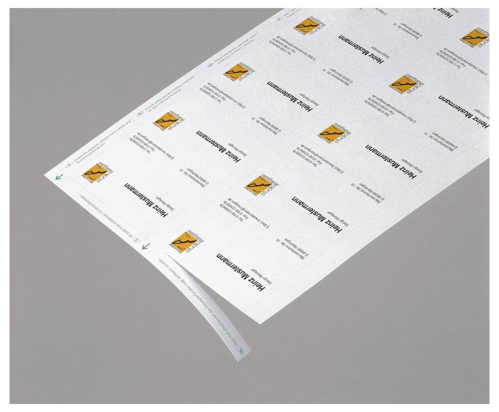 Zwei übereinanderliegende Blätter mit gedruckten Etiketten oder Aufklebern mit einem kleinen orangefarbenen Gefahrensymbol, dargestellt auf grauem Hintergrund.