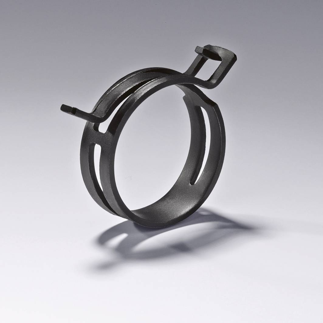 Ein schwarzer Metallclip in runder Form, verwendet zum Fixieren oder Halten von Schläuchen oder Kabeln, mit zwei kleinen, herausstehenden Haken.