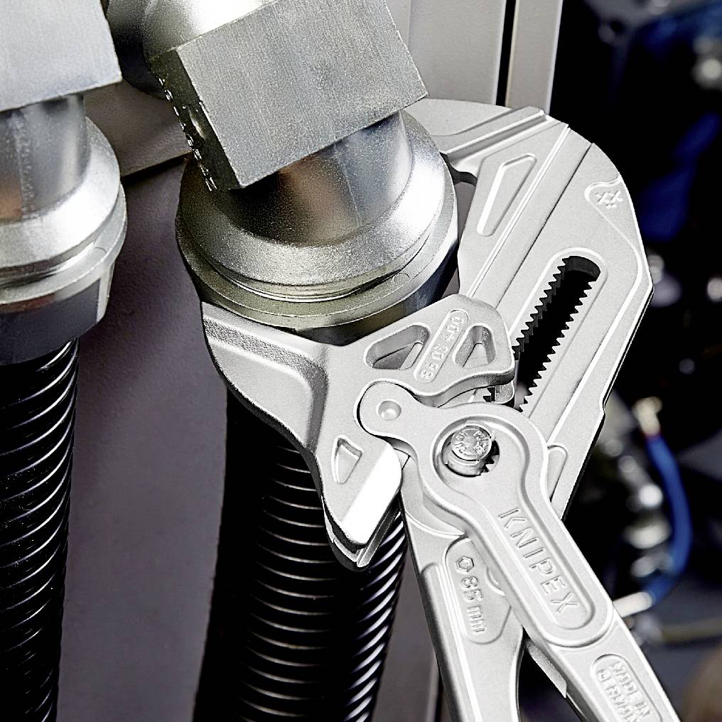 Eine Rohrzange greift ein Metallrohr neben einem weiteren Rohr. Beide Rohre sind mit Armaturen verbunden. Werkzeugeinsatz im Fokus.