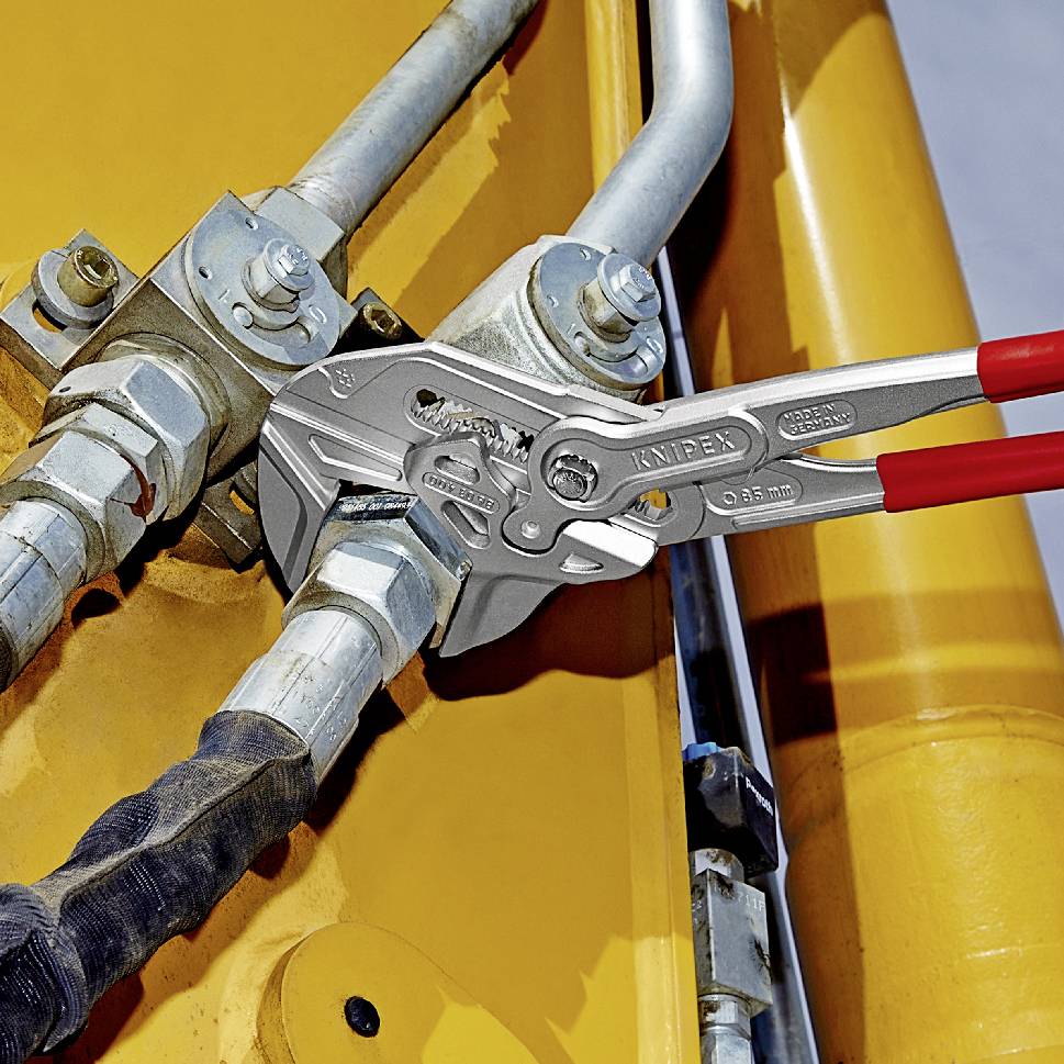 Rohrzange greift Metallverschraubung an gelbem Hydrauliksystem. Werkzeug und Bauteile im Fokus, zeigt technische Anwendung.