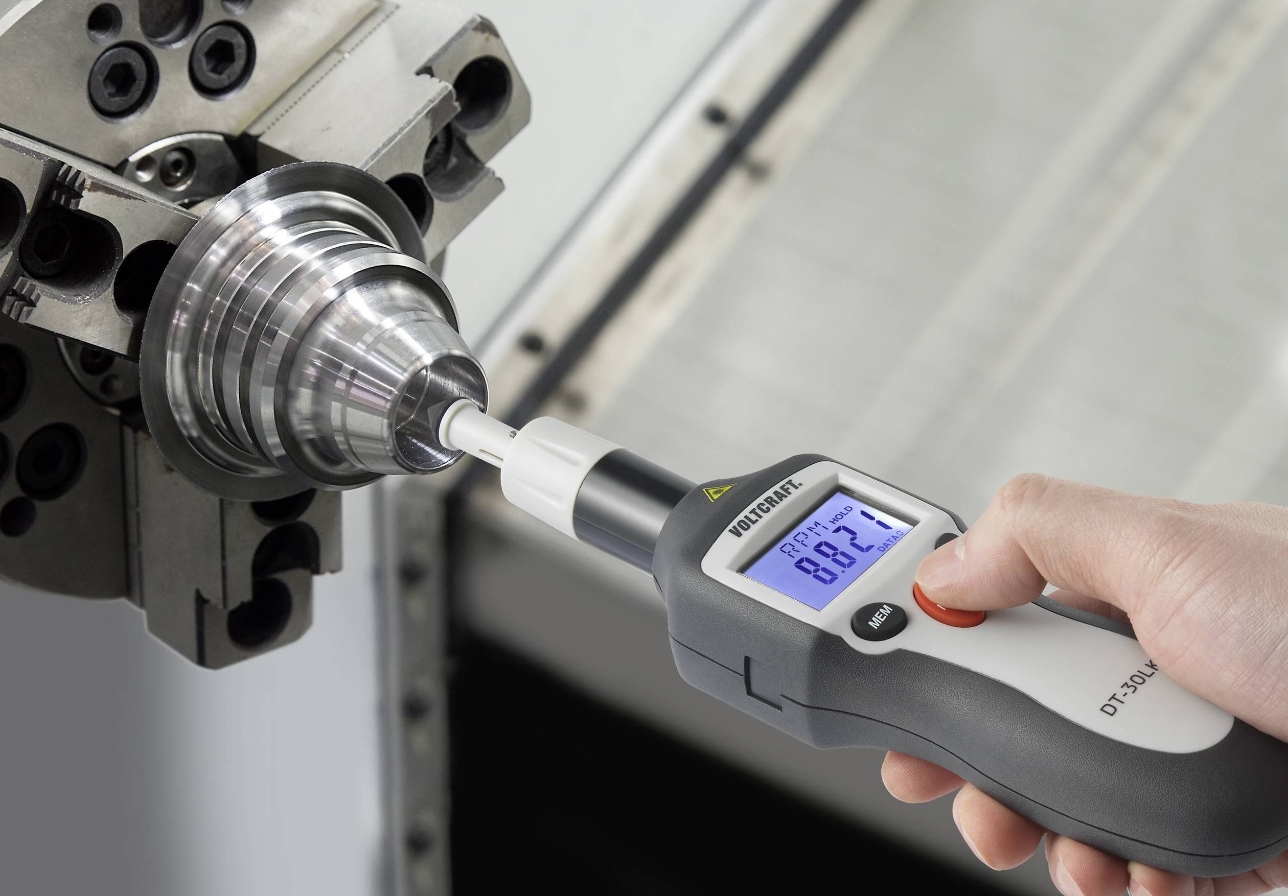 Eine Hand hält ein Werkzeug-Prüfgerät und misst den Rundlauf eines Metallfertigungsstücks, das in einer Maschine eingespannt ist.