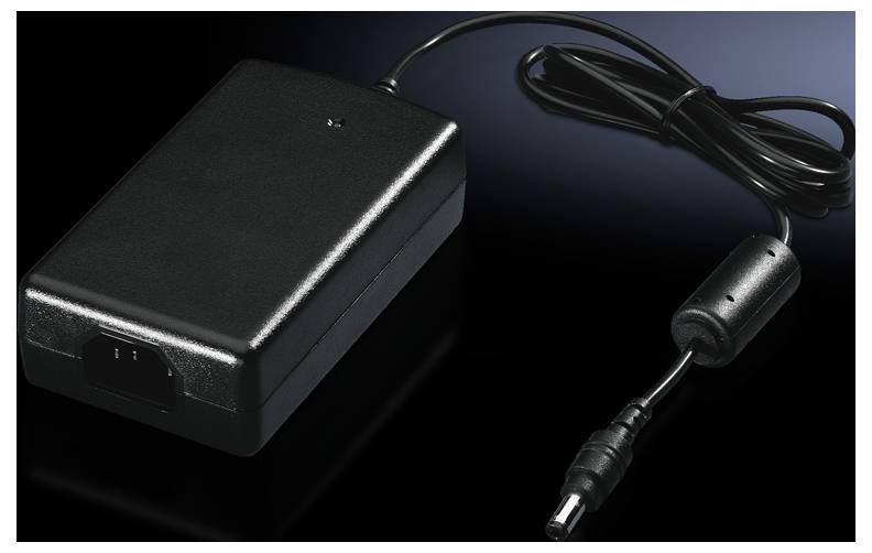 Ein schwarzes Netzteil mit Kabel und Stecker auf dunklem Hintergrund, zur Stromversorgung elektronischer Geräte.