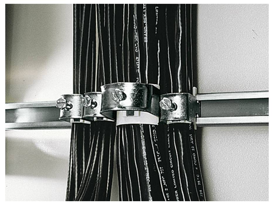 Mehrere schwarze Kabel sind mit Metallklammern an einer Metallstange befestigt. Die Klammern halten die Kabel ordentlich zusammen.
