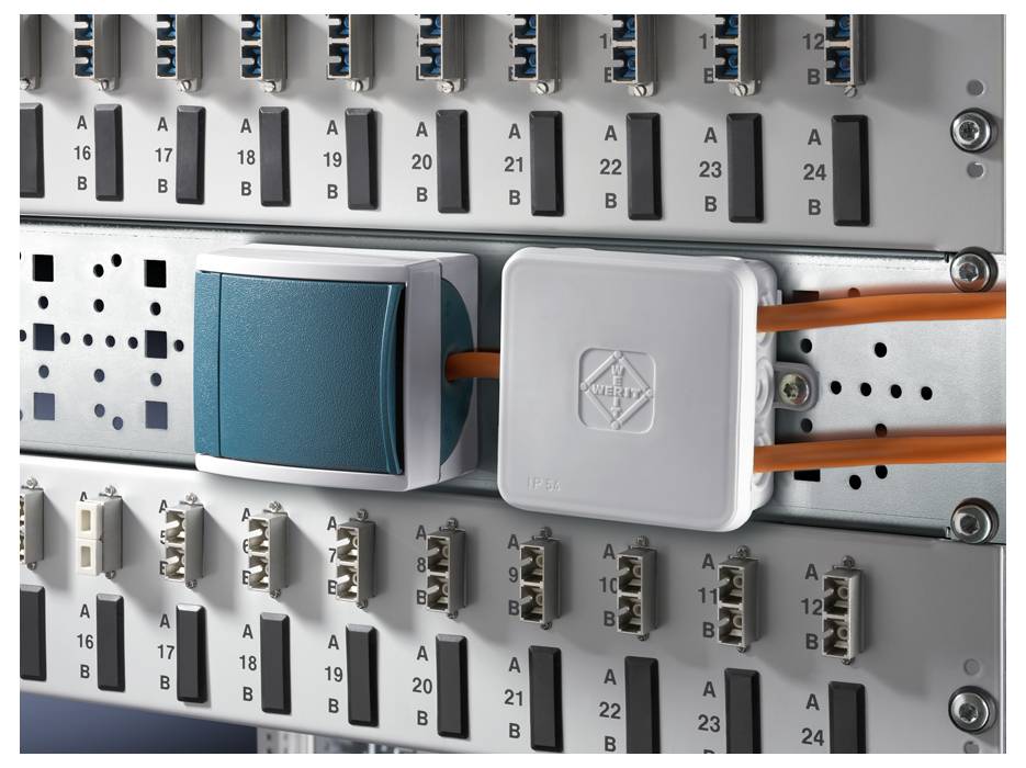 Ein Schaltschrank mit elektronischen Anschlüssen, Kabeln und Steckverbindungen. Ein grünes und ein graues Modul sind sichtbar eingesteckt.