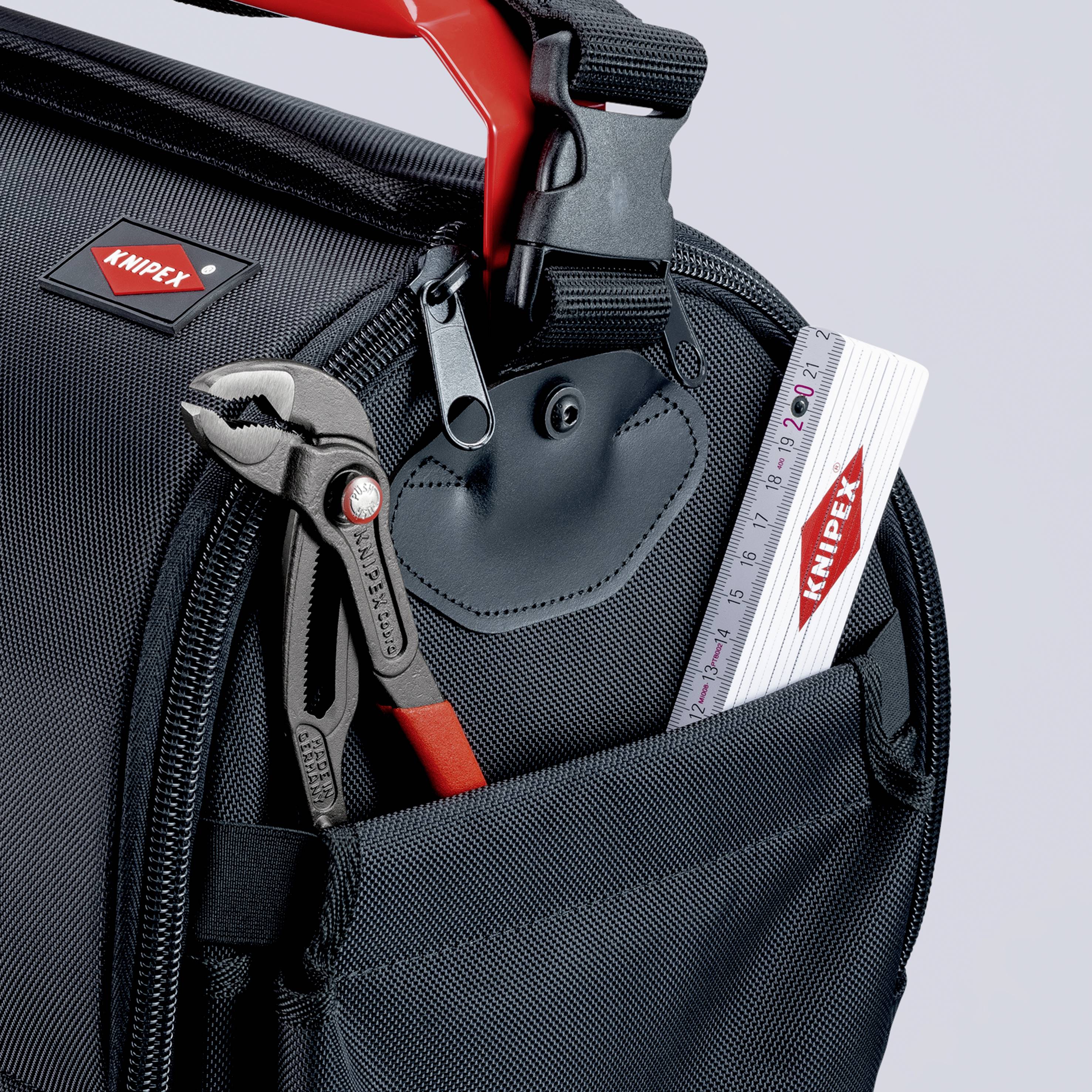 Eine schwarze Werkzeugtasche mit einem verstellbaren Rotgriff, eine Schraubzange und ein weißer Knipex-Zollstock im vorderen Fach.