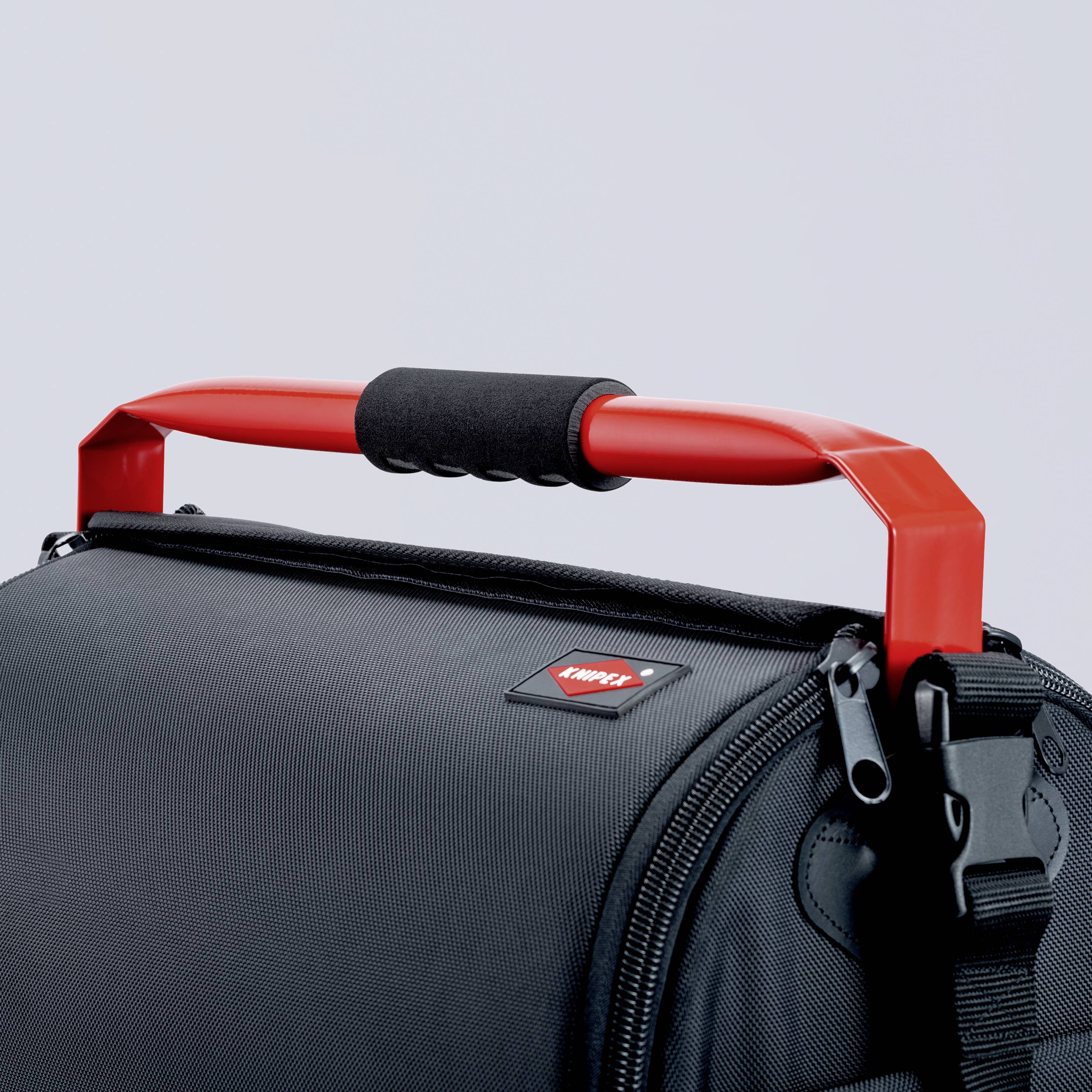 Nahaufnahme einer schwarzen Tasche mit einem roten Griff. Der Fokus liegt auf dem robusten Design und dem Kontrast zwischen Farbe und Material.