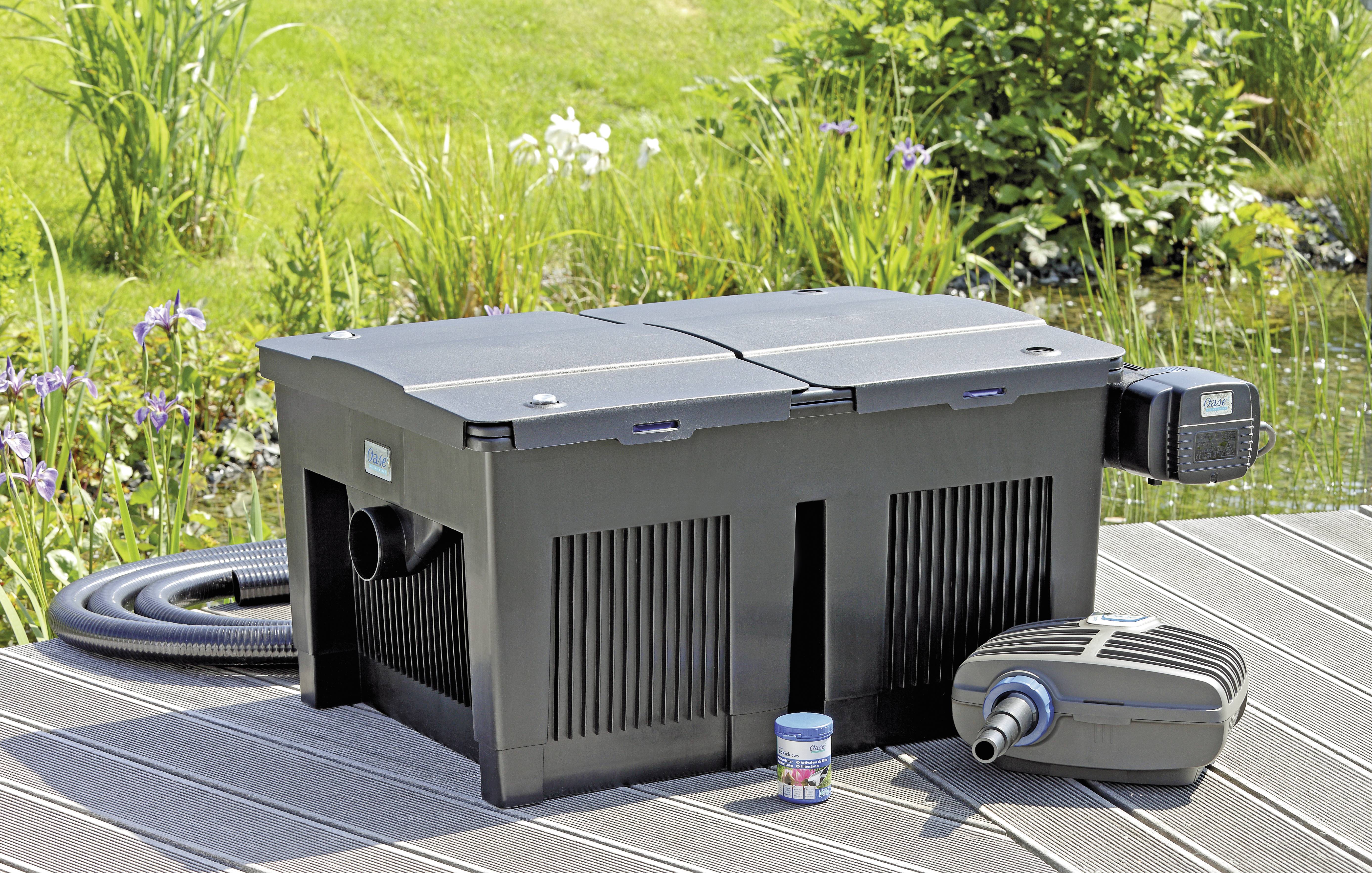 Ein Teichfiltrationssystem im Freien, aufgestellt auf Holzterrassenbrettern neben einem Teich. Beinhaltet eine große Filterbox, eine Luftpumpe und einen Verbindungsschlauch.