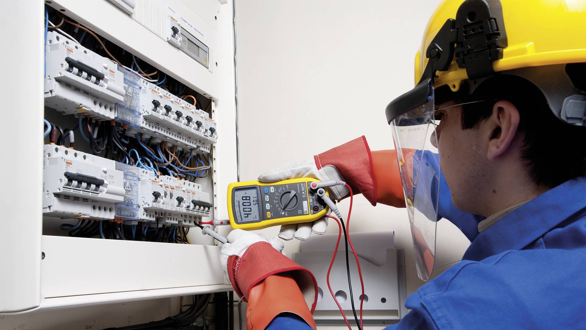 Ein Techniker mit Schutzhelm überprüft mit einem Multimeter den elektrischen Schaltkasten.