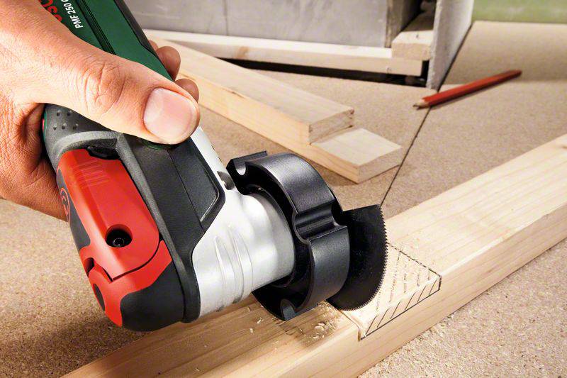 Eine Hand hält ein elektrisches Multitool, das ein rechteckiges Muster in ein Holzstück schneidet.