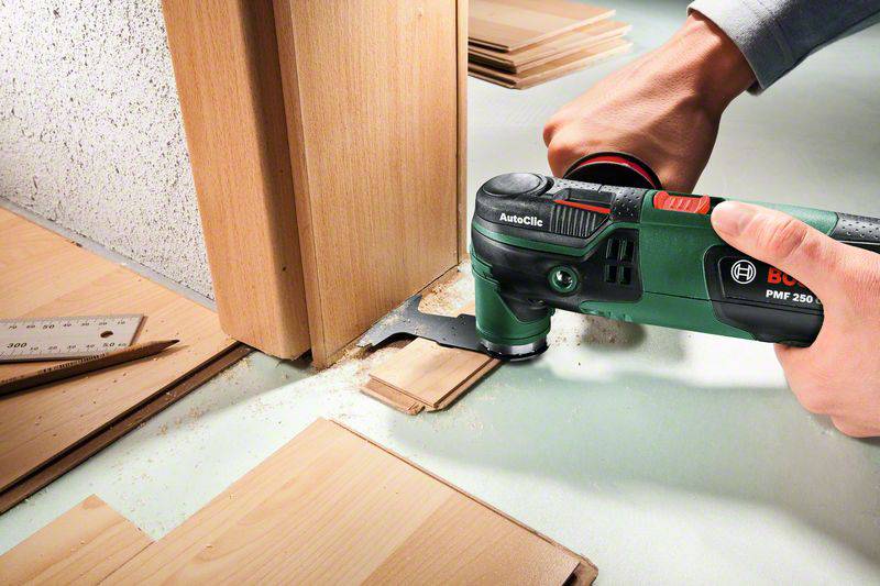 Eine Person schneidet Holz mit einem oszillierenden Multifunktionswerkzeug an einem Türrahmen. Es sind Holzspäne zu sehen.