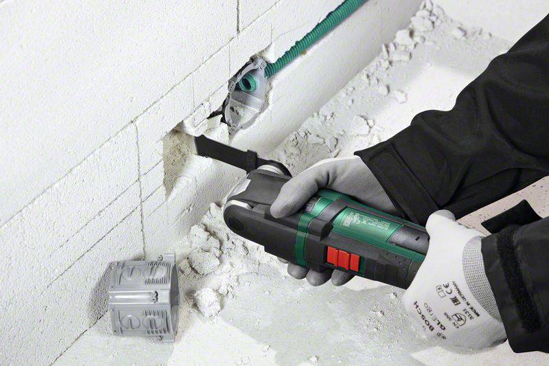 Eine Person schneidet mit einem oszillierenden Werkzeug eine gerade Linie in eine weiße Wand aus Betonformsteinen.