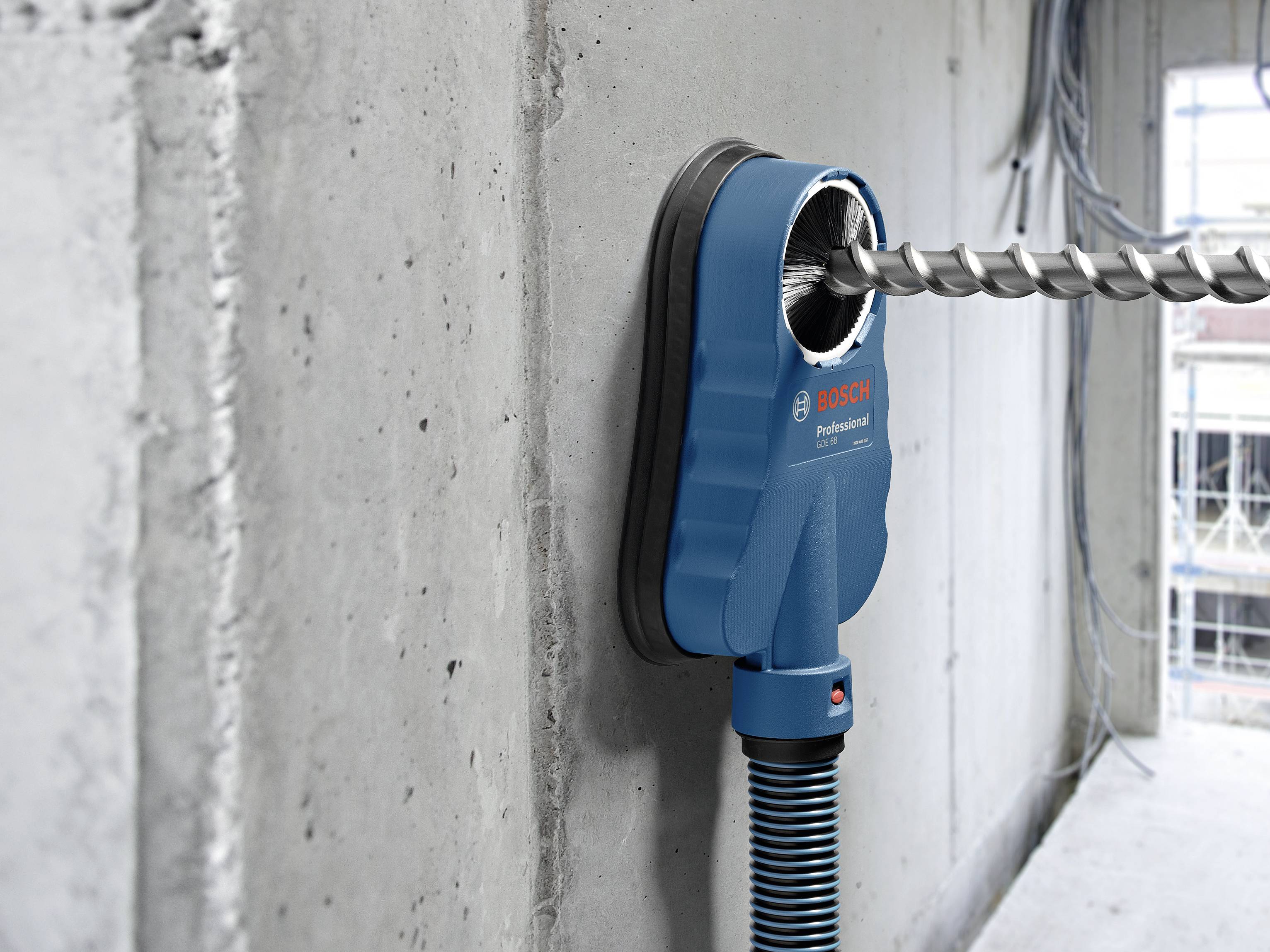 Bohrmaschine mit Staubsaugeraufsatz bohrt ein Loch in eine Betonwand. Staub wird durch den Aufsatz direkt abgesaugt.