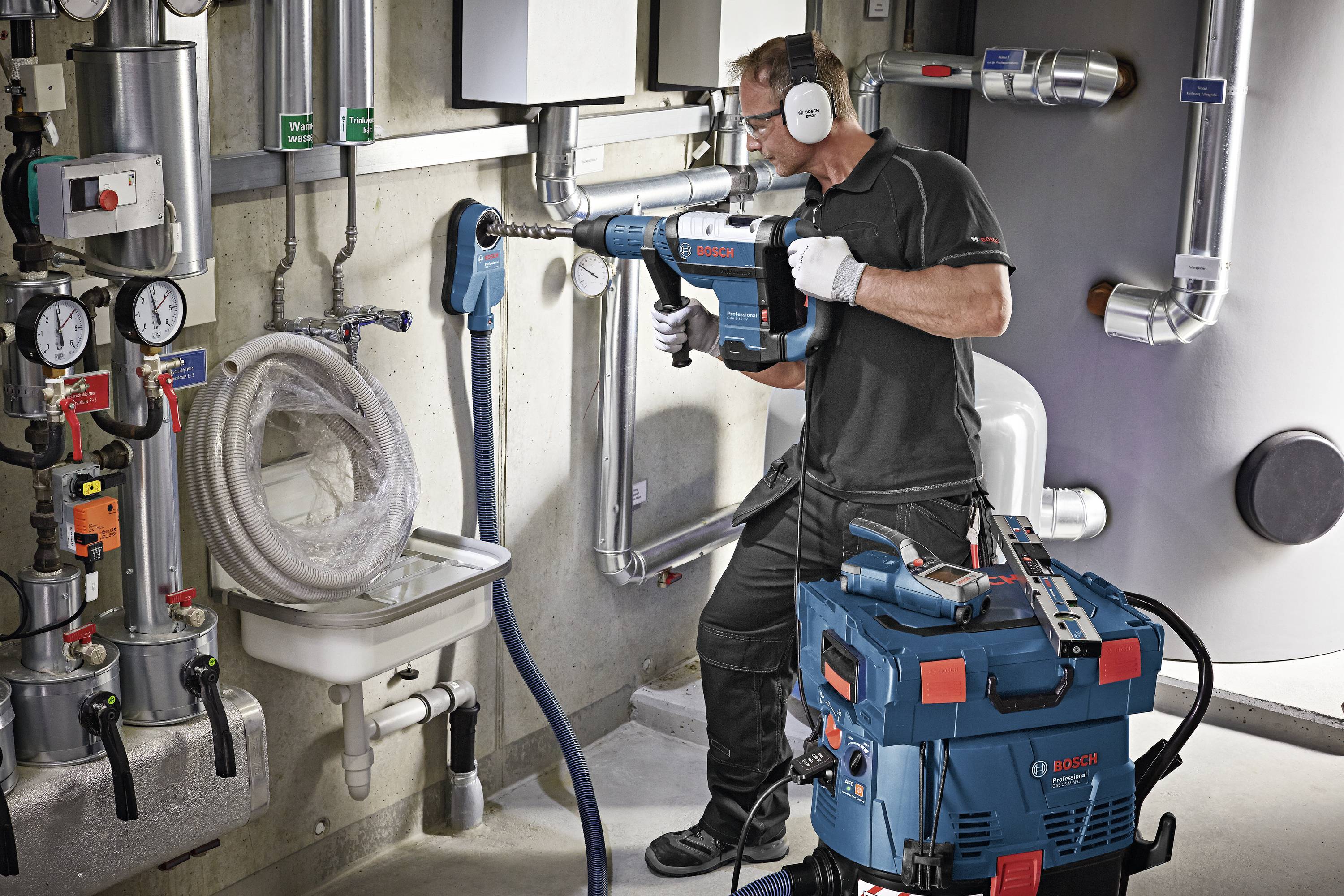 Ein Techniker in einer Werkstatt verwendet ein elektrisches Werkzeug von Bosch. Im Hintergrund sind Rohre und Messgeräte zu sehen.