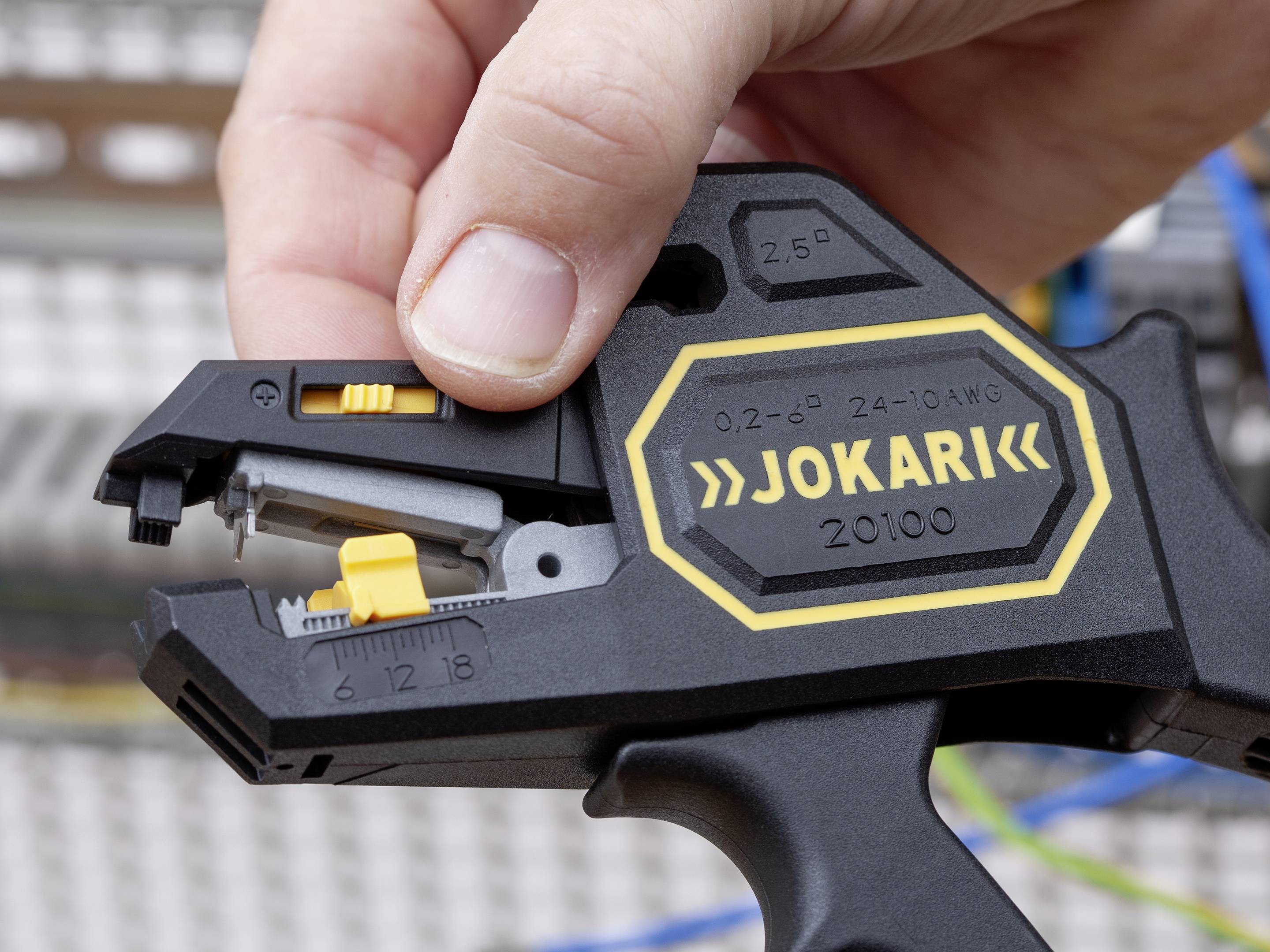 Ein Handwerkzeug für Kabelabisolierung wird von einer Hand gehalten. Auf dem Werkzeug steht 'Jokari' mit Spezifikationen dazu.