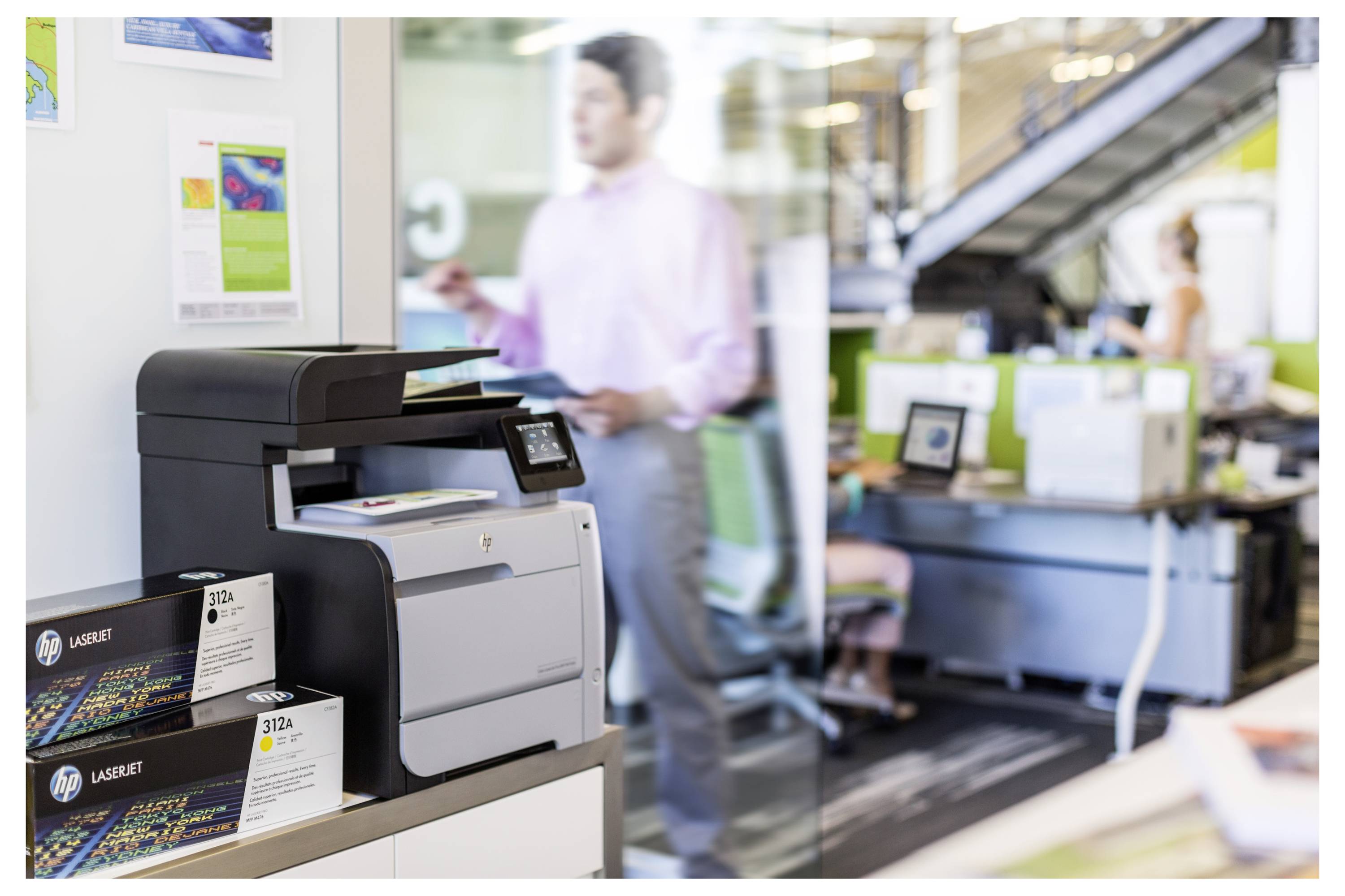 HP LaserJet Drucker auf einem Ausstellungstisch in einem Büroausstellungsraum, mit Produktkarten und Menschen, die im unscharfen Hintergrund arbeiten.