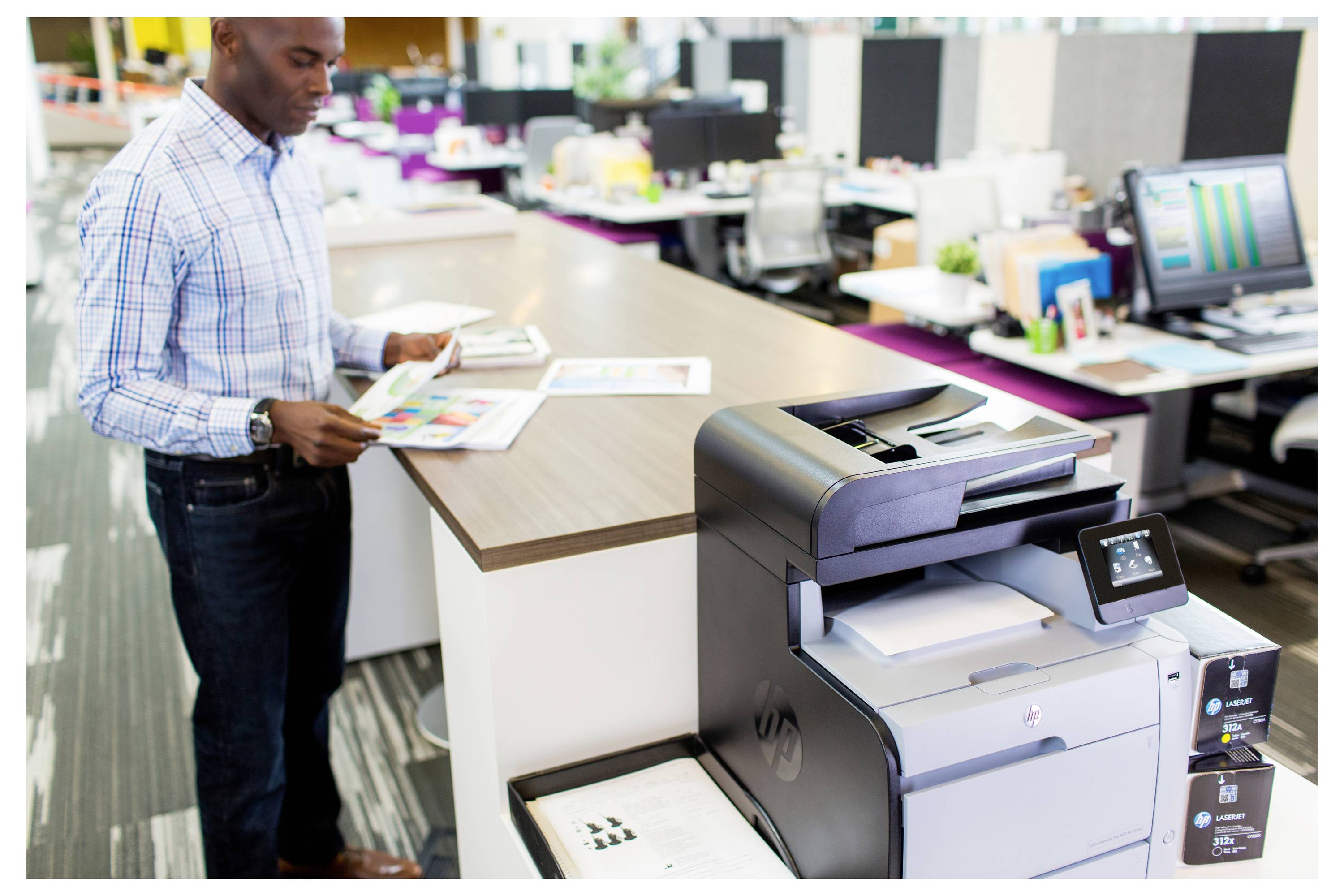 Büroangestellter überprüft Dokumente neben einem großen Multifunktionsdrucker/Kopierer in einem geschäftigen Büroarbeitsbereich.