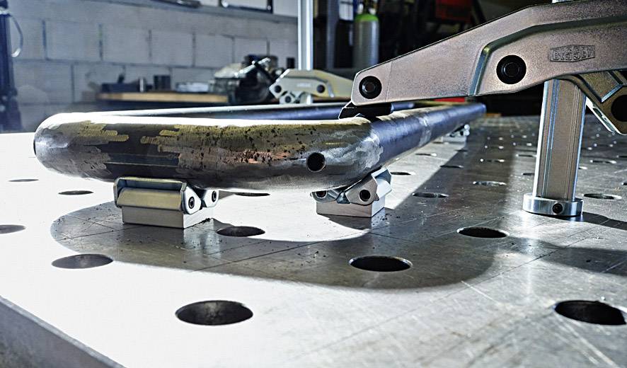 Nahaufnahme eines Metallrohrs, das auf einem Werkstatttisch mit Metallklammern fixiert ist. Im Hintergrund sind Werkzeuge sichtbar.