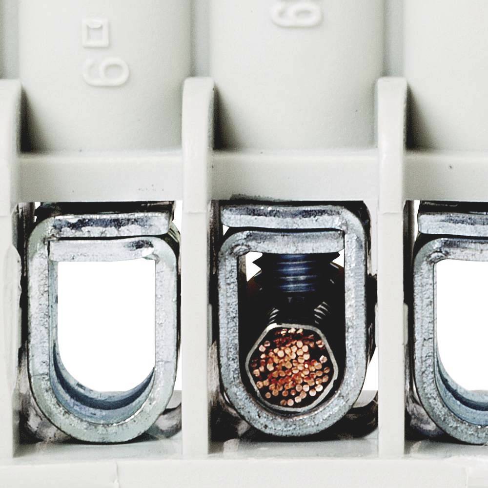 Nahaufnahme eines elektrischen Anschlussklemmenblocks mit sichtbaren Kupferdrähten im Inneren einer terminalen Schraubverbindung.
