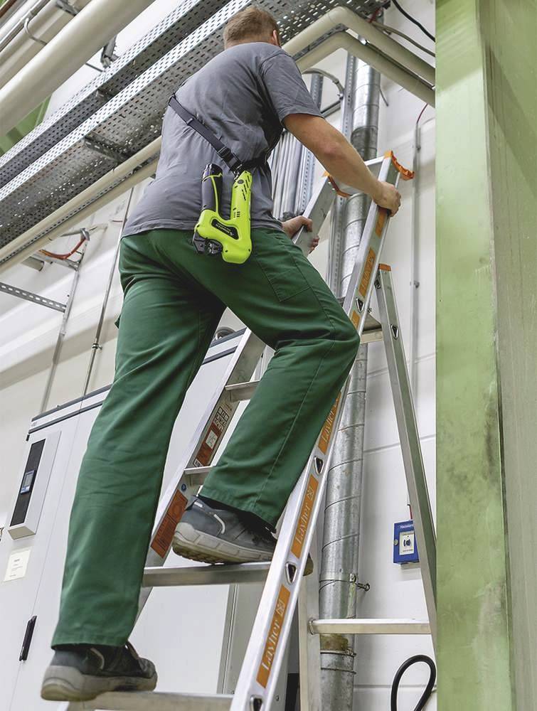 Ein Arbeiter steigt eine Leiter hinauf, um Rohrleitungen in einer industriellen Umgebung zu inspizieren. Der Arbeiter trägt Sicherheitskleidung.