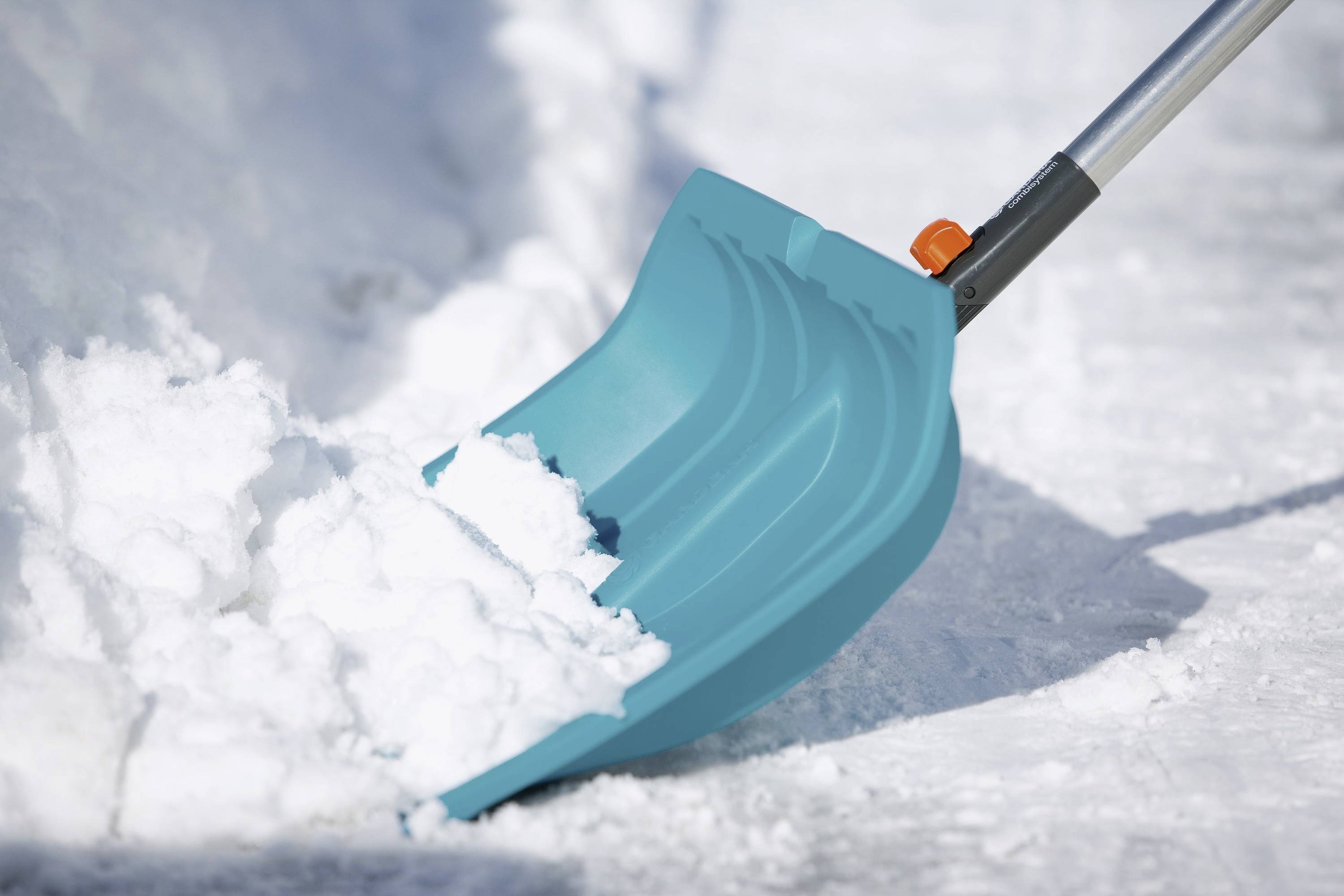 Eine blaue Schneeschaufel bewegt Schnee von einem Gehweg. Der Fokus liegt auf der Schaufel mit einem Hintergrund aus weißem Schnee.