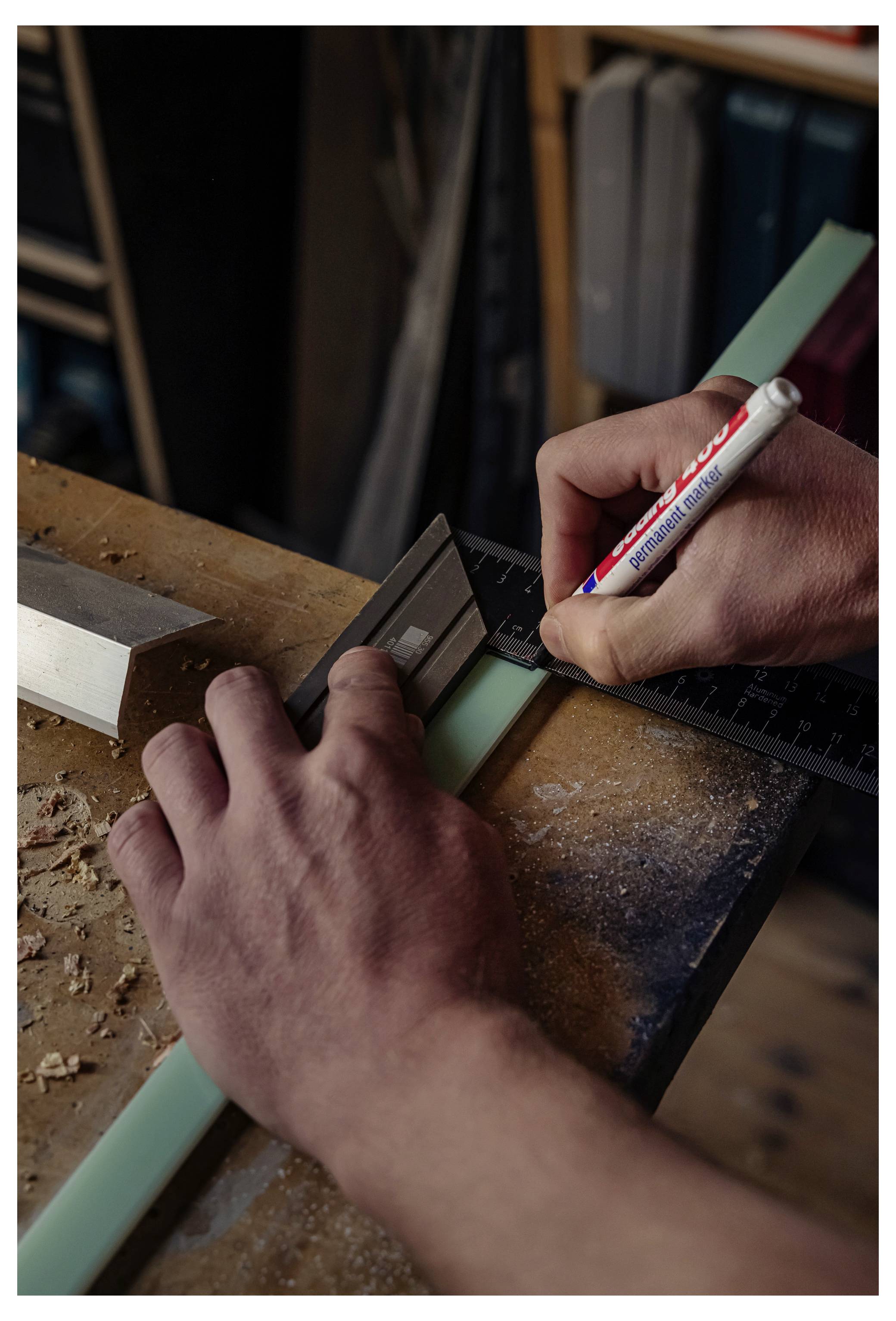 Hände, die ein Lineal und einen Bleistift verwenden, um einen mintgrünen Streifen auf einer Werkbank während einer Holzbearbeitungsaufgabe zu messen und zu markieren.