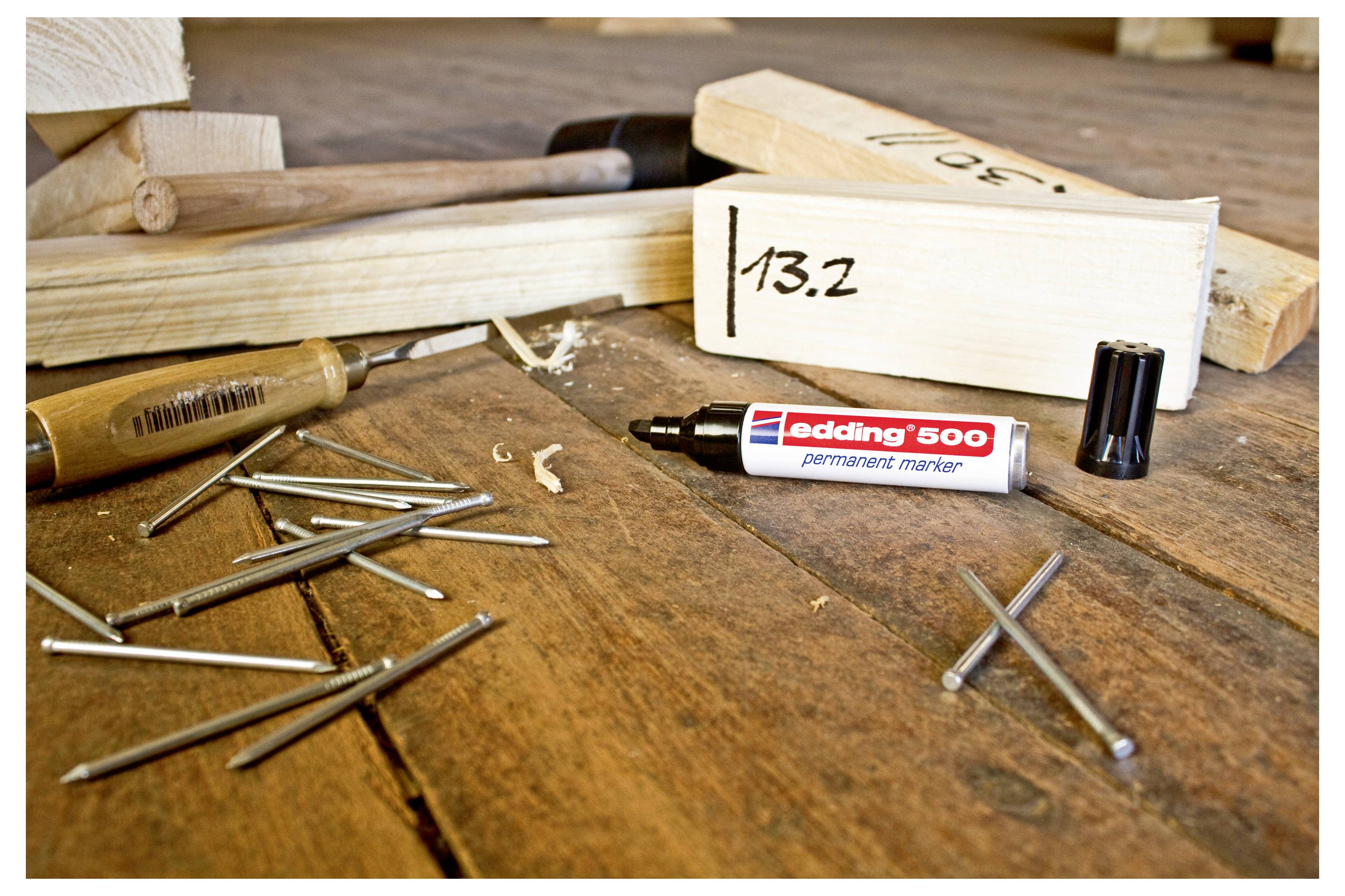 Holzbearbeitungswerkzeuge auf einer Werkbank, darunter ein Hammer, Nägel, ein Bohrer und ein Marker mit der Bezeichnung „edding 500"; ein Holzblock ist mit „13,2" gekennzeichnet.