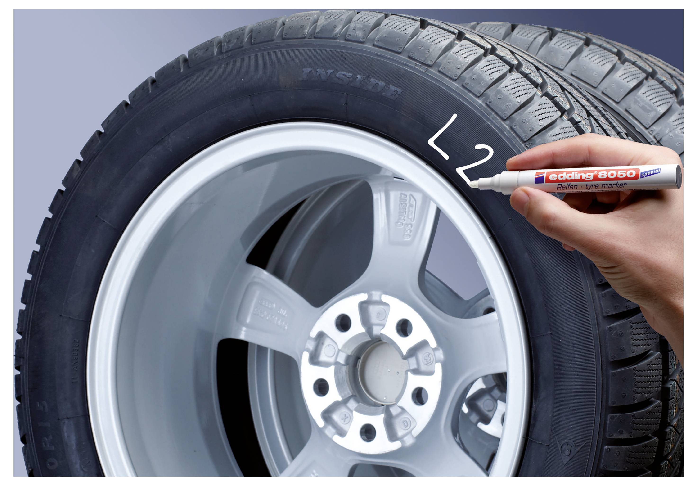 Handschrift "L2" auf einer Autoreifen-Seitenwand mit weißem Marker geschrieben, Nahaufnahme von Rad und Felge.