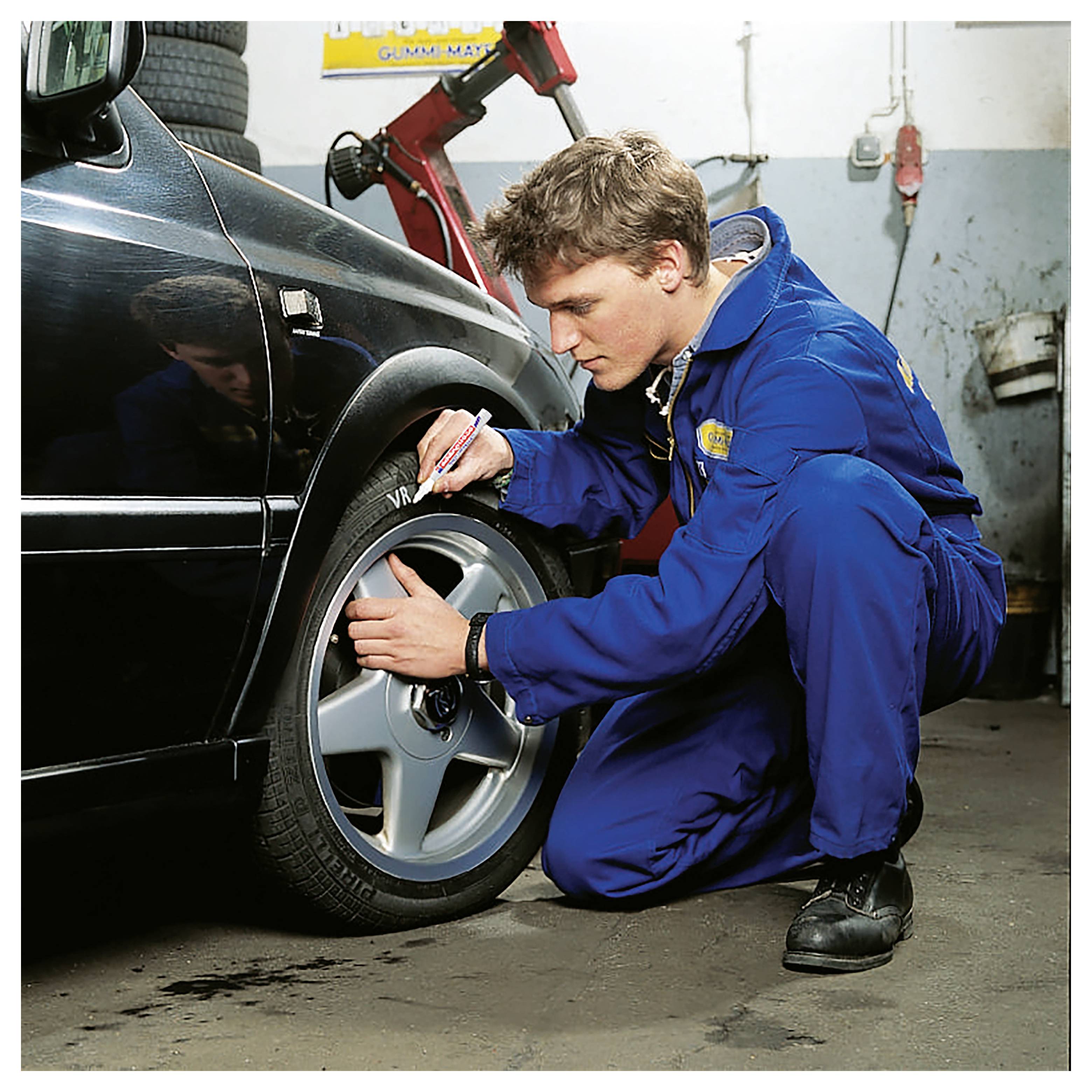 Mechaniker in blauen Overalls überprüft und markiert einen Autoreifen in einer Autowerkstatt.