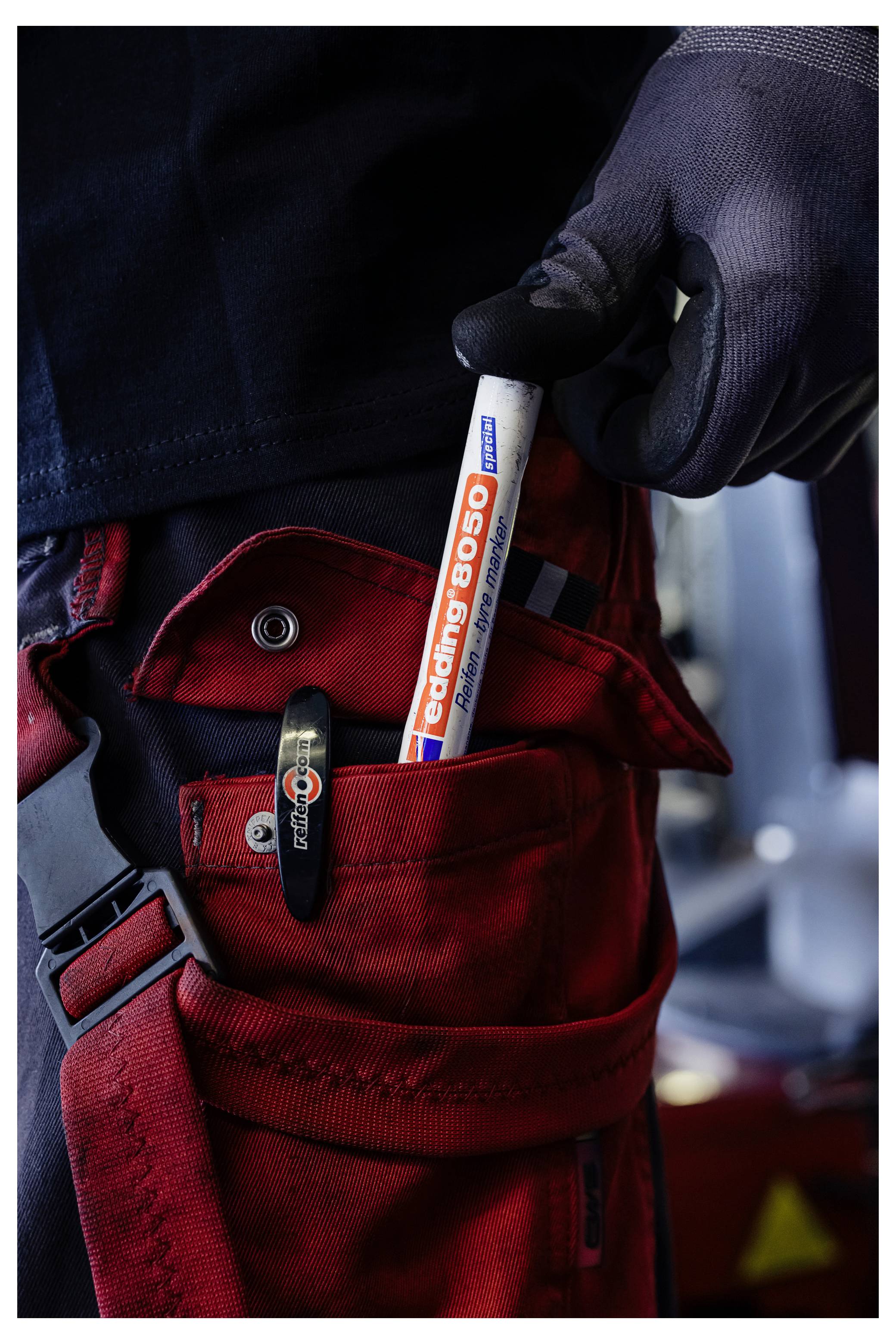 Behandschuhte Hand, die einen "Coling 8050"-Marker über einer offenen roten Werkzeugtasche mit Clip und Druckknopftasche hält.
