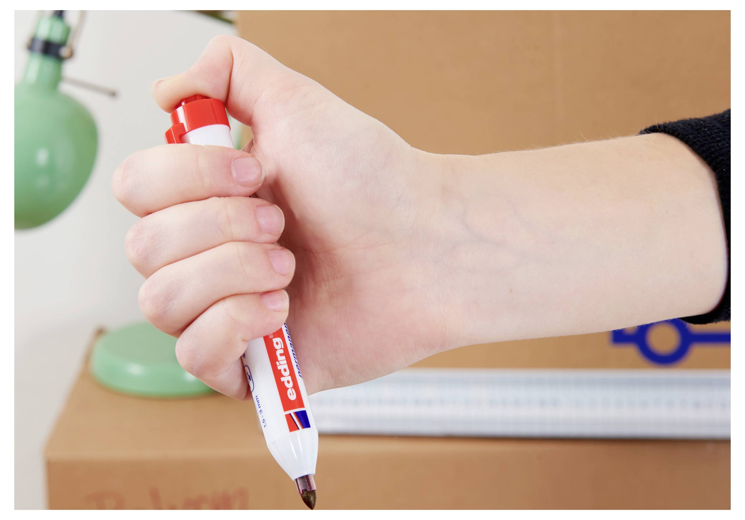Eine Hand hält einen roten Trockenmarker, der bereit ist, auf einem Whiteboard zu schreiben, mit unscharfen Unterrichtsmaterialien im Hintergrund.