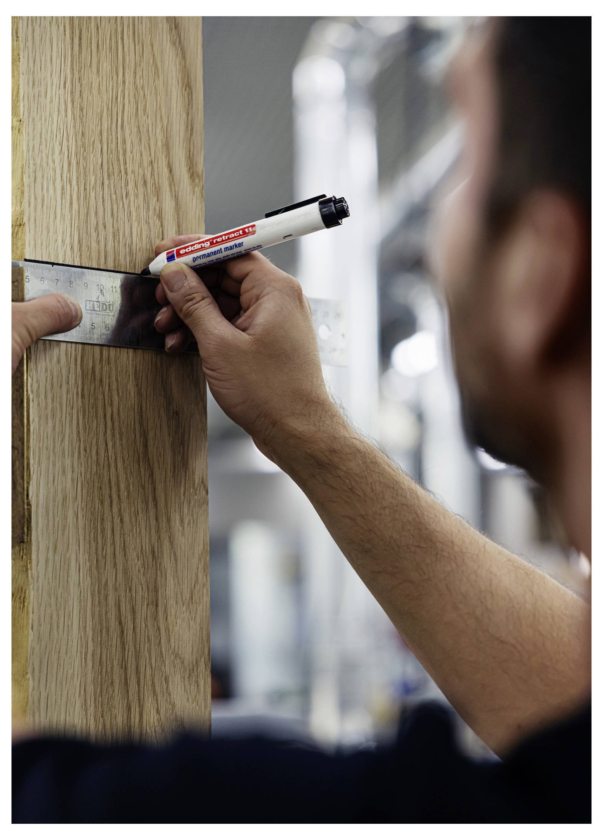 Eine Person markiert während der Schreinerei Messwerte auf einem Holzbrett mit einem Marker und einem Metalllineal.